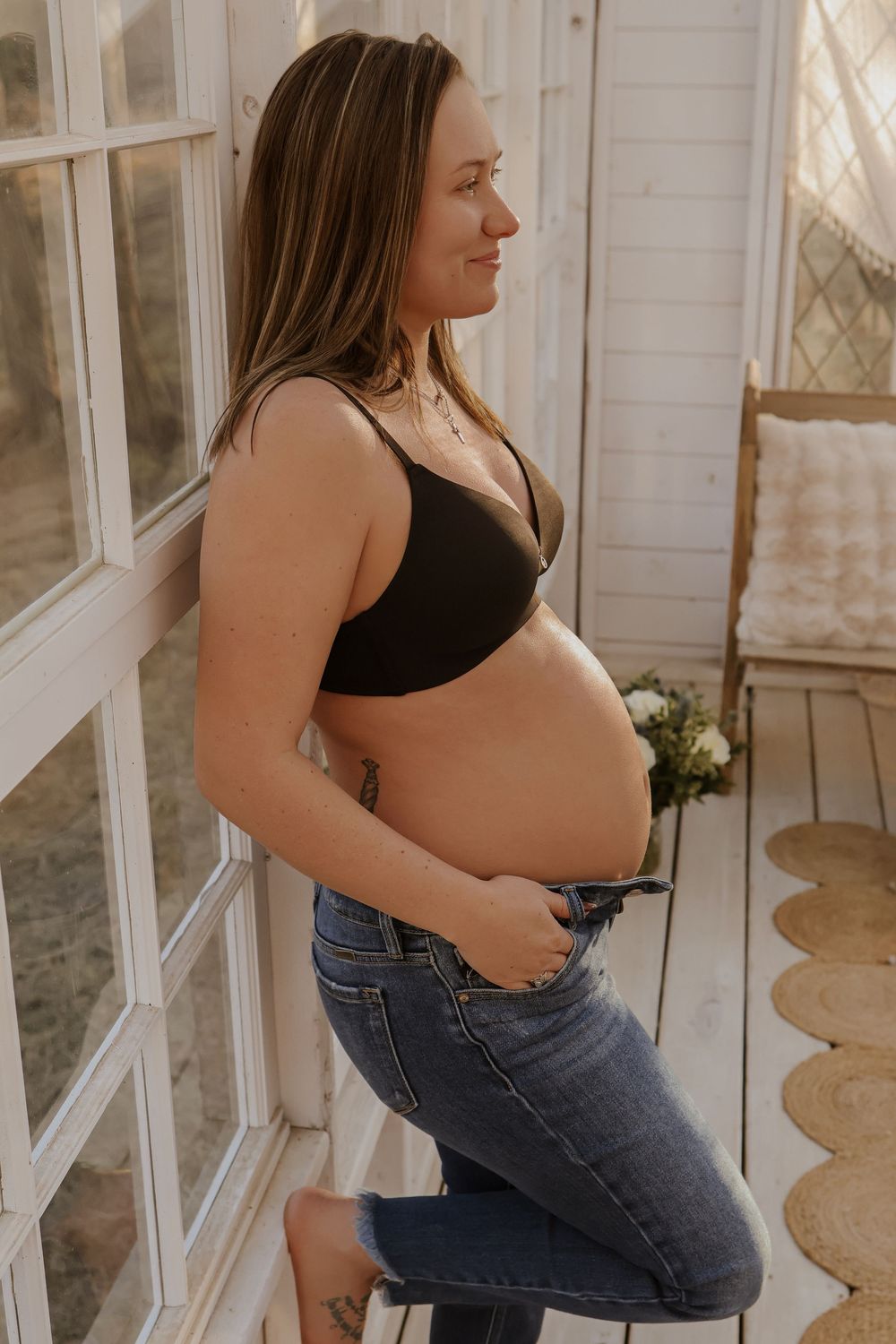 Side view of pregnant belly in black top and jeans by sunlit window.