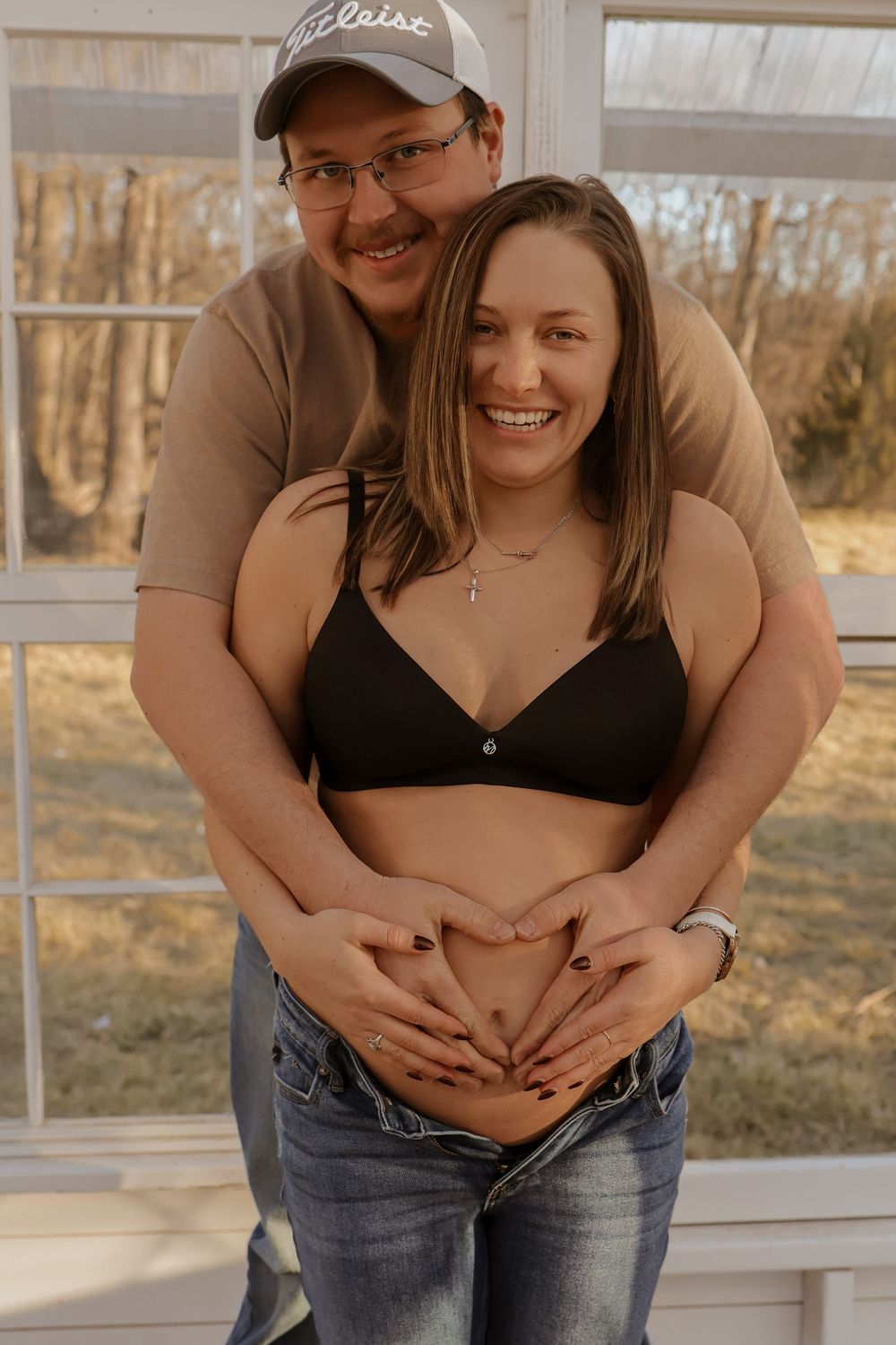 A couple embracing during a pregnancy announcement photoshoot in casual attire.