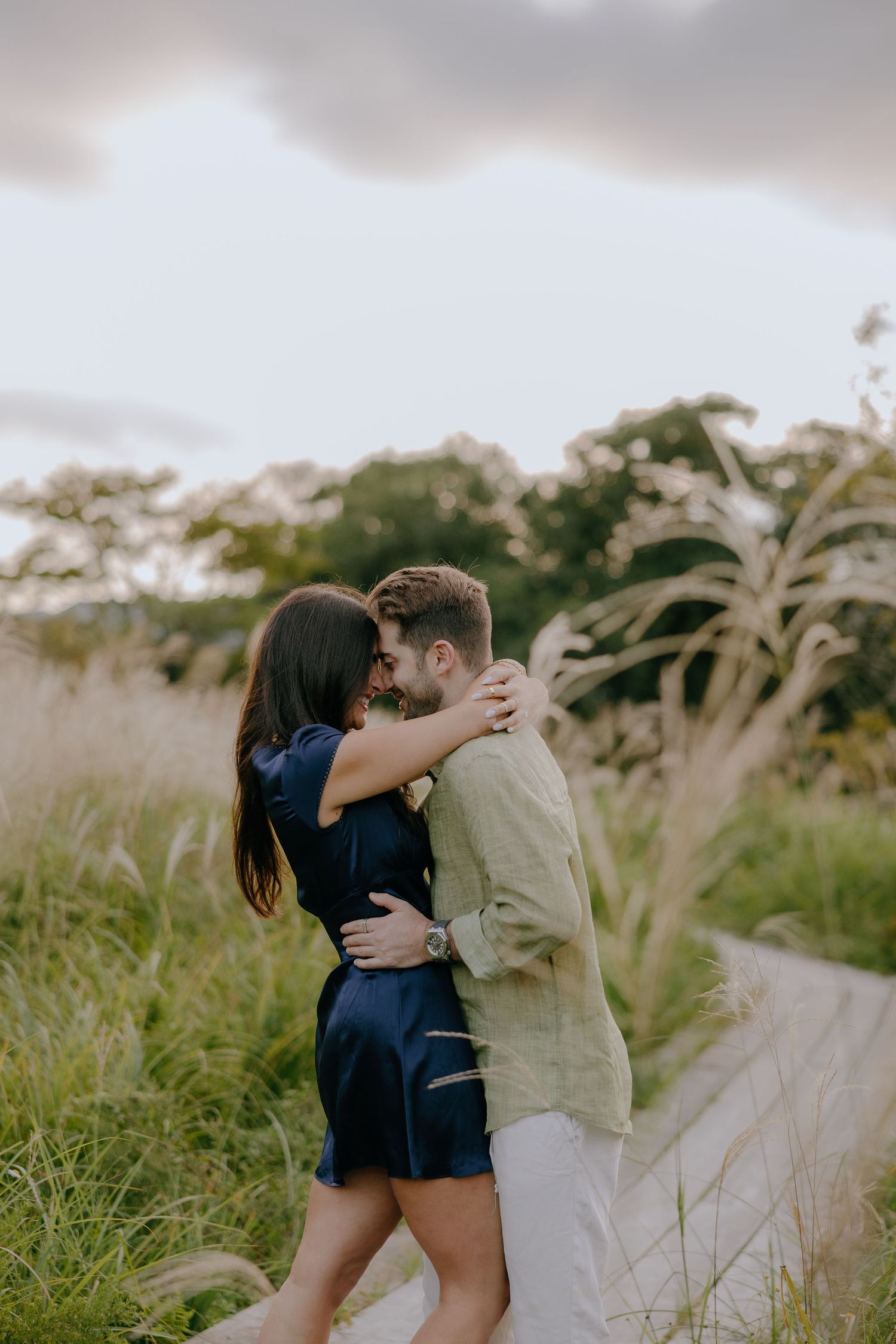 A romantic couple embraces in a field of tall grass during golden hour.