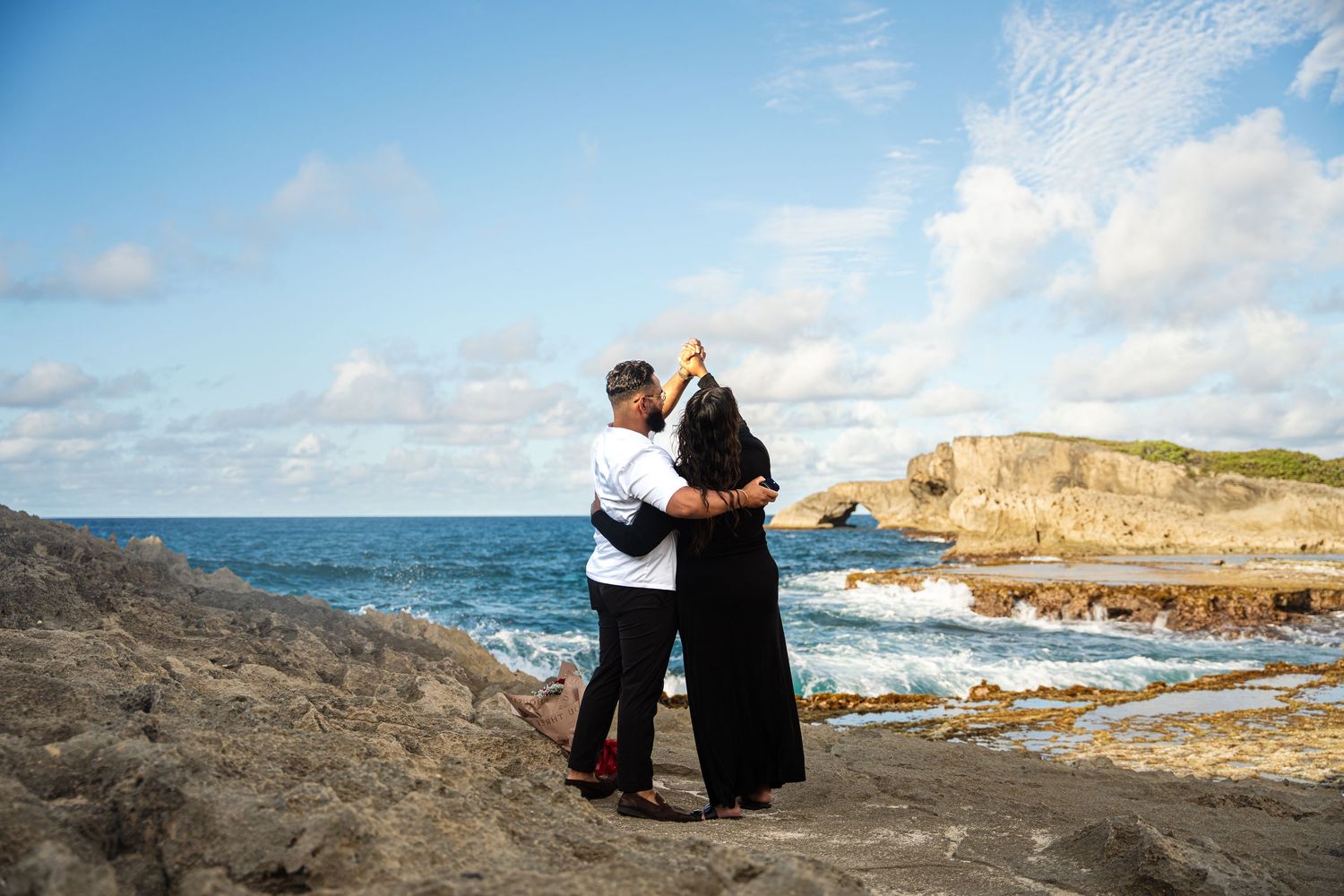 Couple enjoying scenic coastal views along rocky cliffs and ocean landscape during sunset.