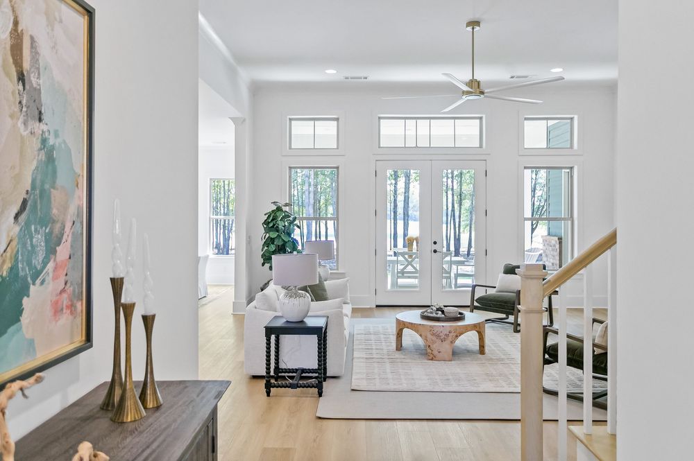 Bright modern living room with white walls, abstract art, and natural light streaming through tall windows.