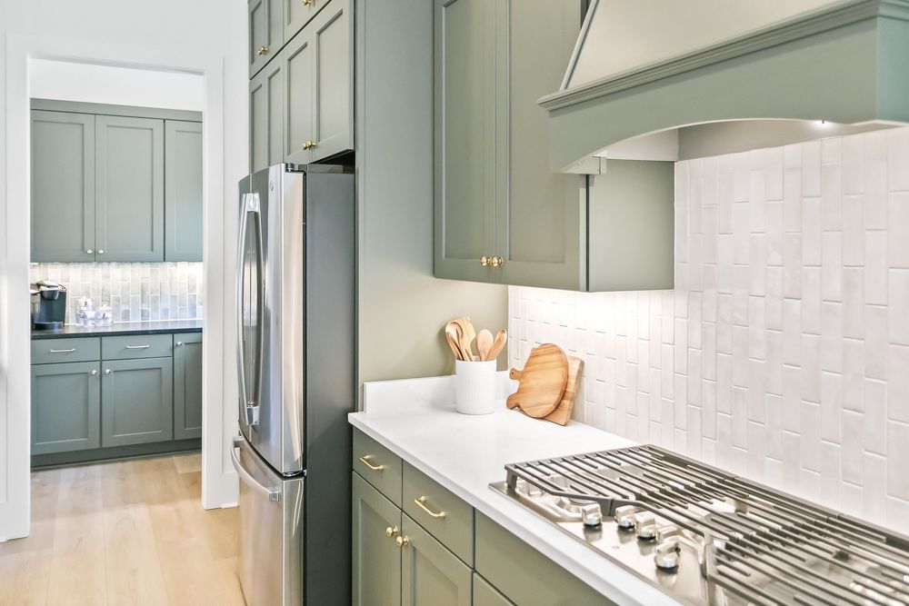 Modern kitchen features sage green cabinets, white subway tile backsplash, and stainless steel appliances.