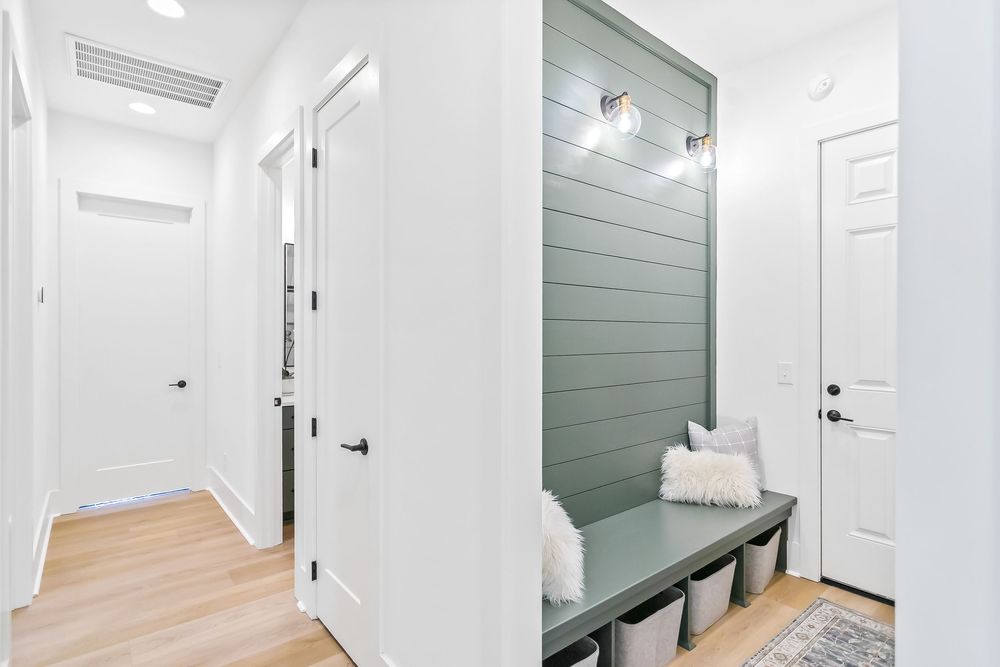 Modern hallway with white walls, light wood flooring, and sage green accent wall features multiple doorways.
