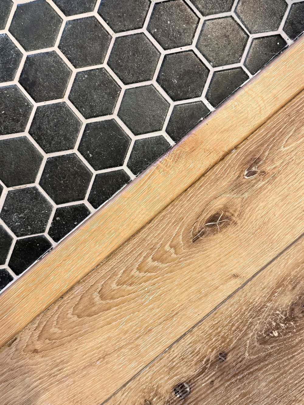 Close-up of hexagonal black tile flooring meeting natural wood planks with visible grain pattern.