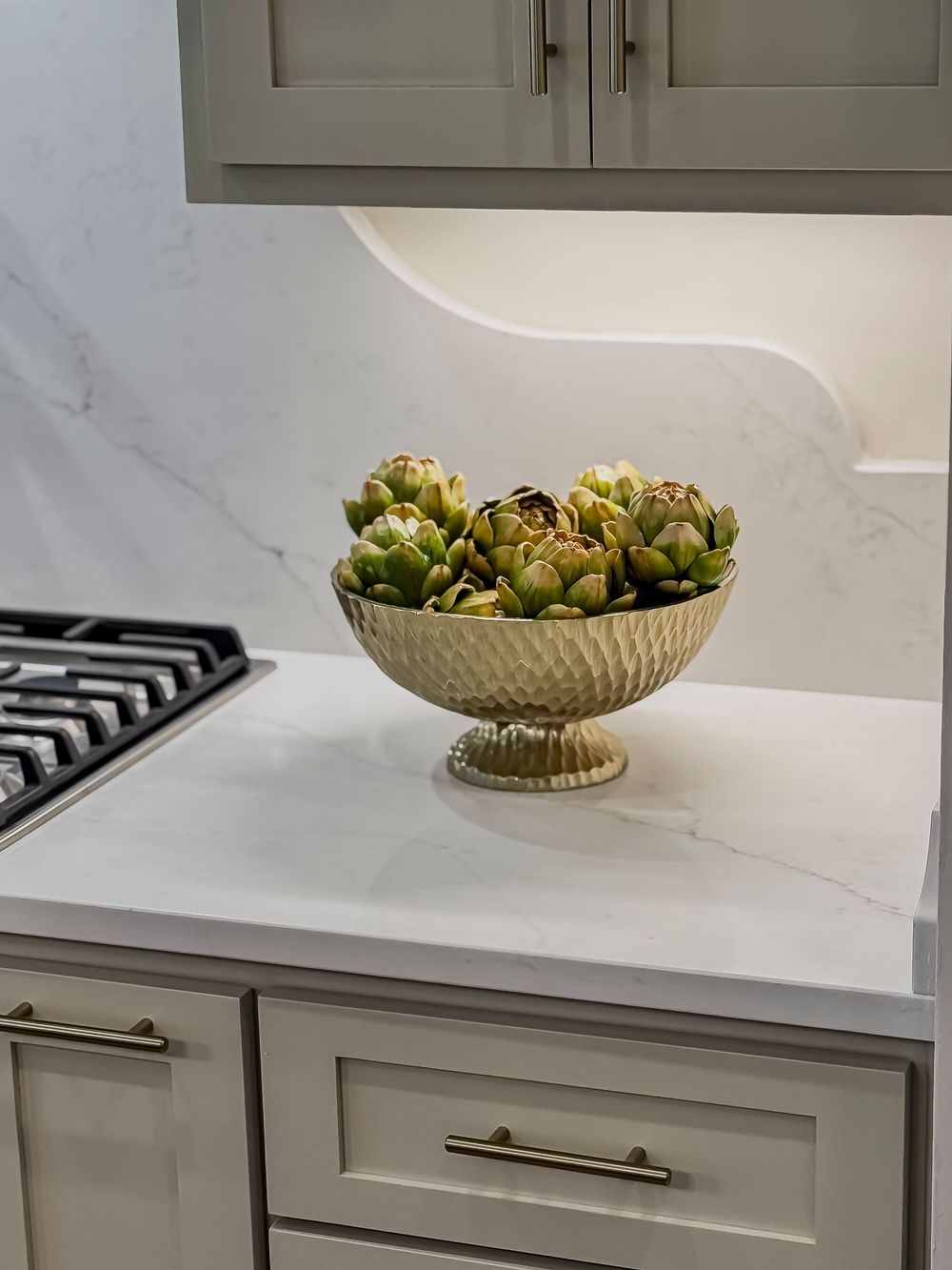 White marble countertop with gray cabinets and decorative bowl containing artichokes.