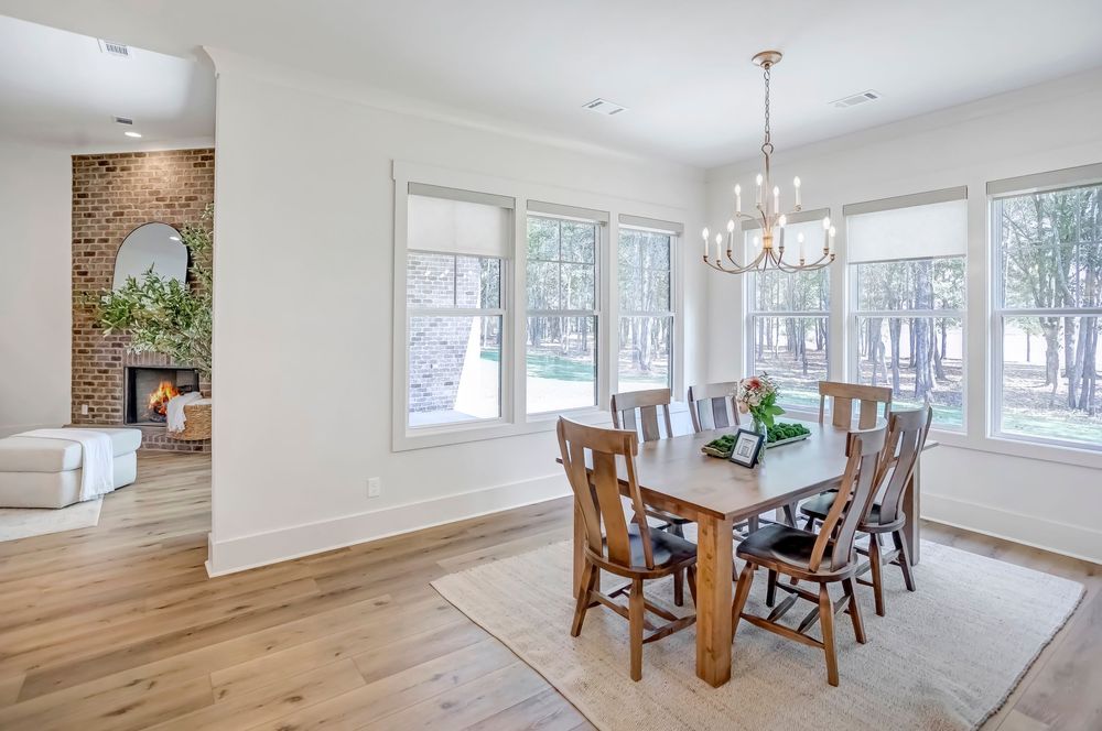Modern dining room features hardwood floors, white walls, and large windows letting in natural light.
