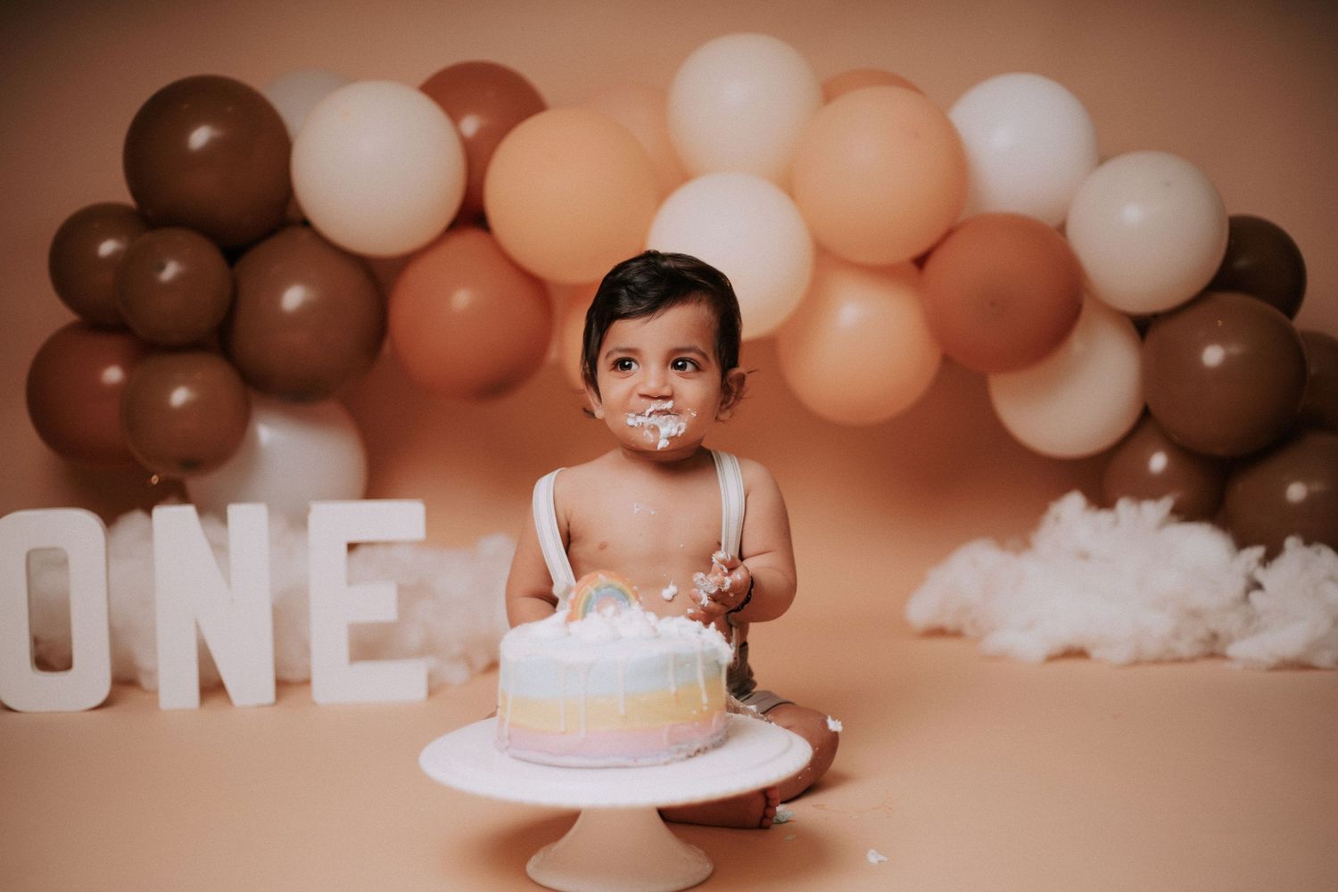 Minimalist cake smash photography setup with earth-toned balloons and 'ONE' lettering.