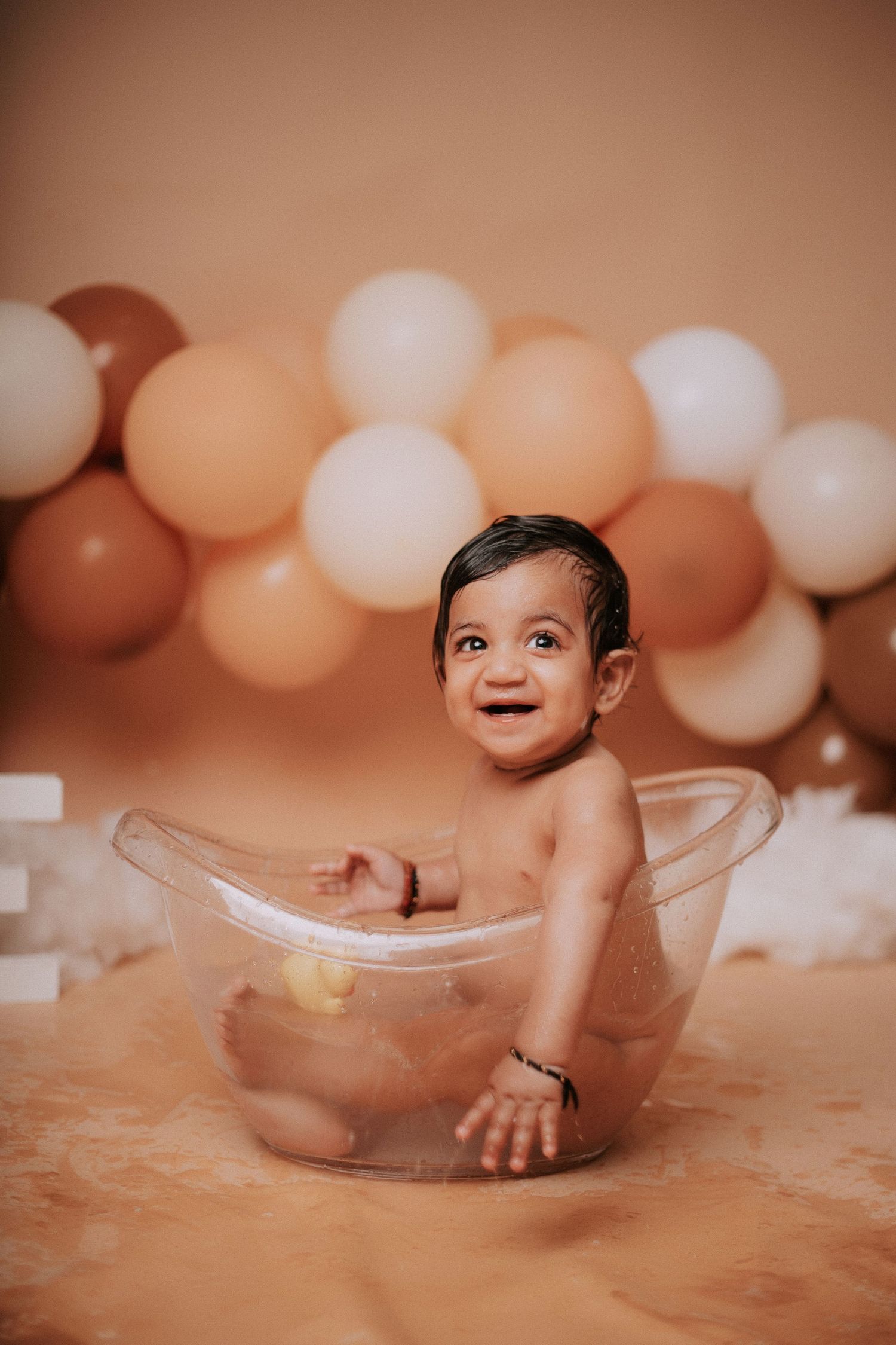 First birthday photoshoot with clear tub prop and elegant balloon decor in warm tones.
