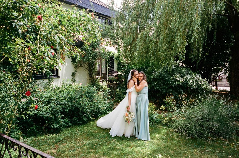 Wedding party in light blue dresses walks through a lush garden setting with weeping willow trees.