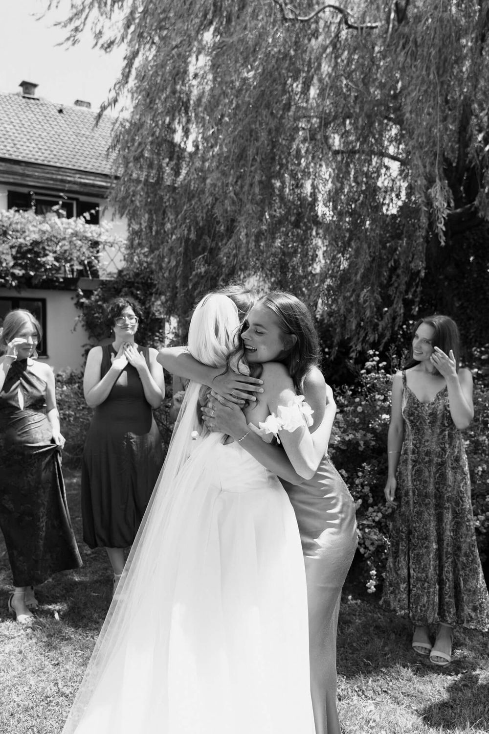 A bride in a flowing white wedding dress spins playfully under a weeping willow tree in a garden setting.