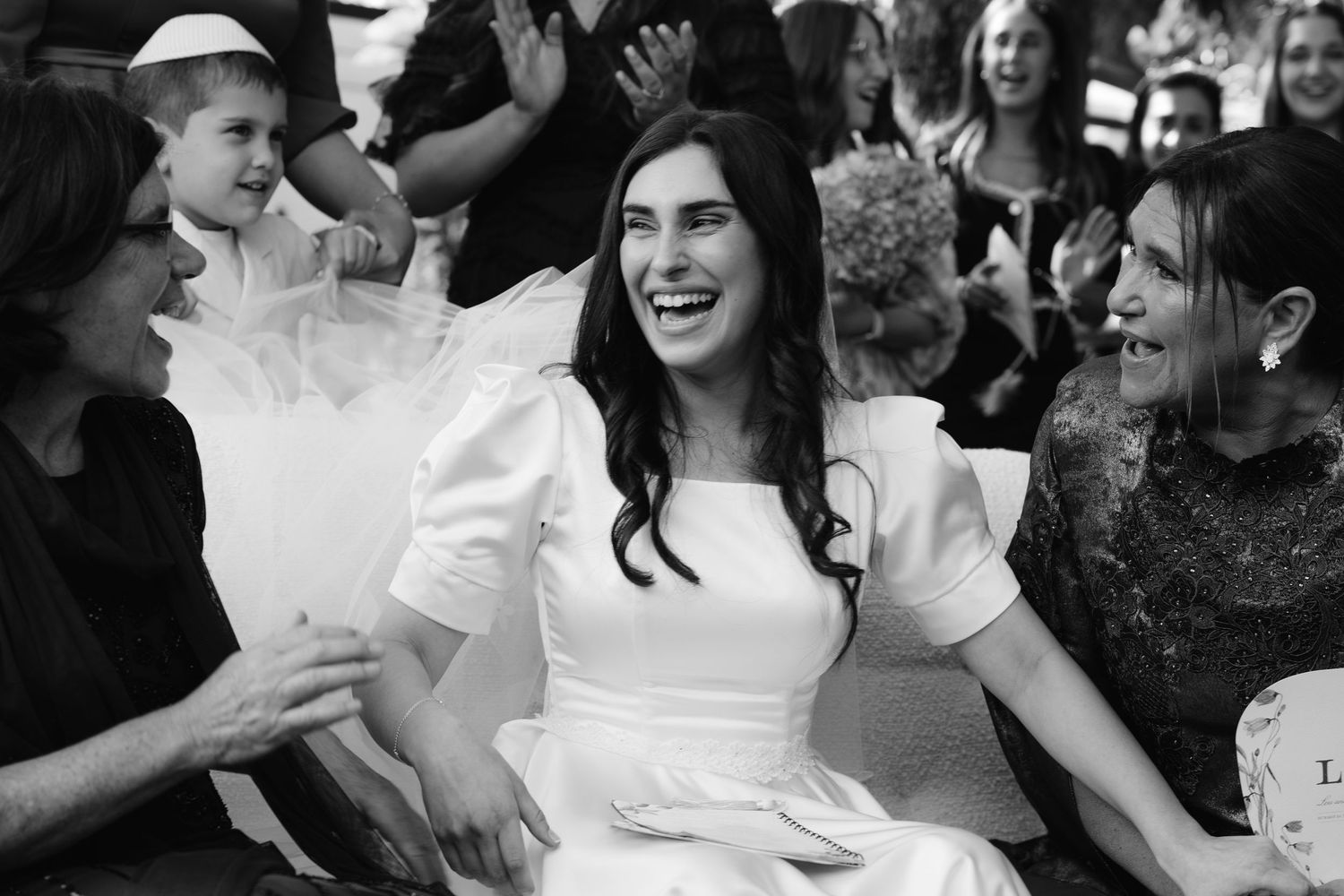 Black and white photo showing a joyful celebration at a wedding reception with dancing and laughter.