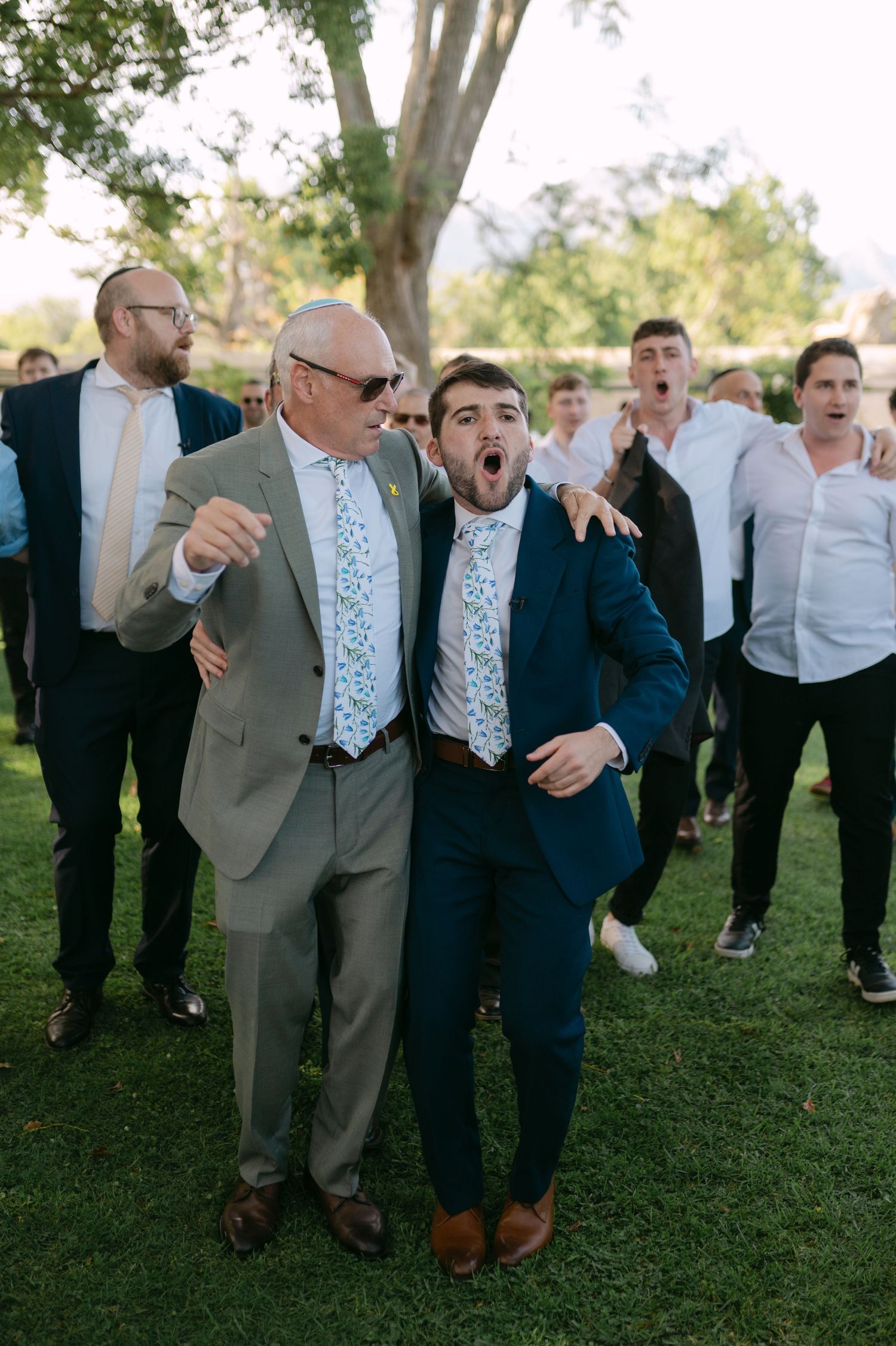 Wedding guests enjoying a fun, candid moment together on a grassy lawn at an outdoor celebration.