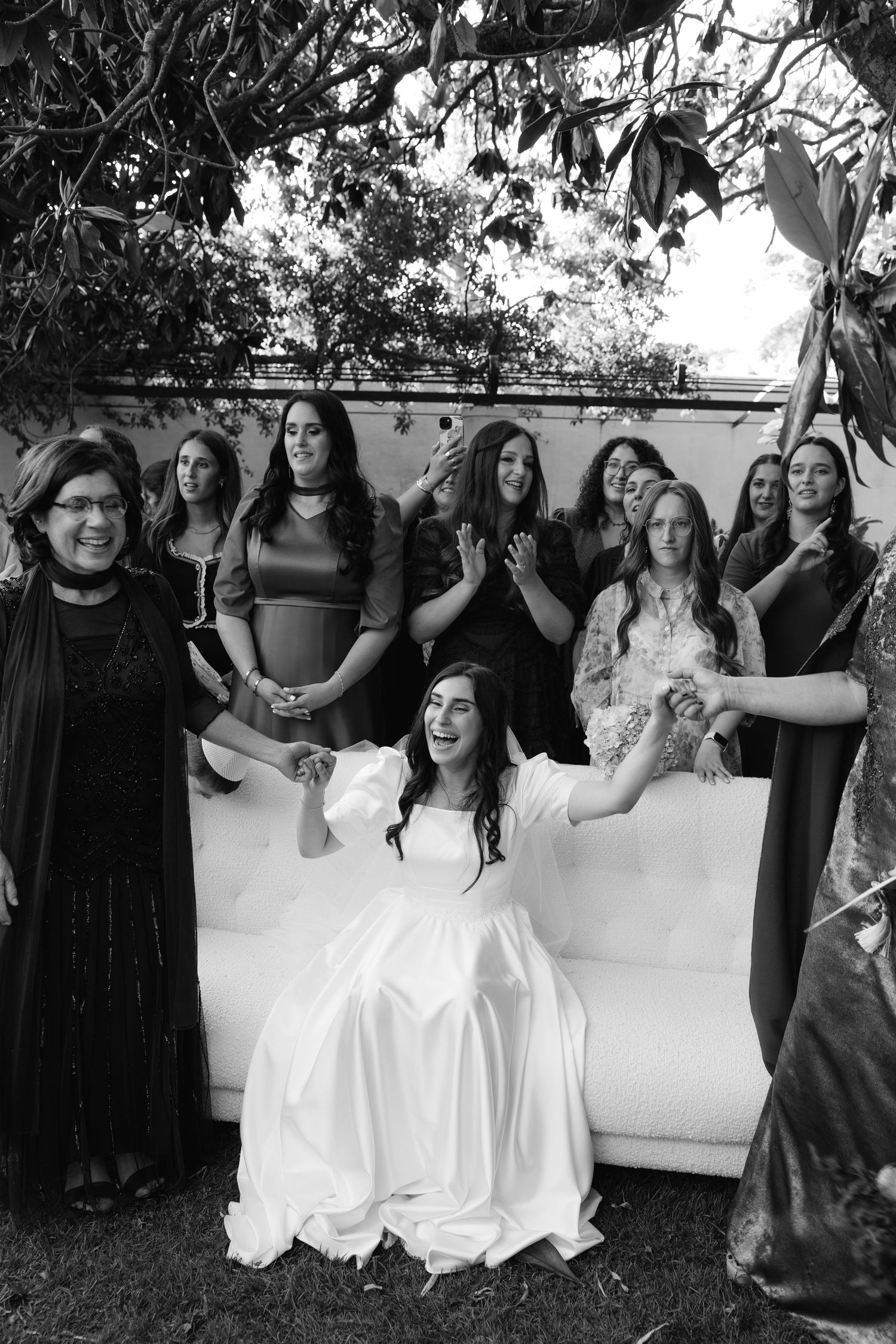 Wedding party members in black and white dresses share candid laughing moments during outdoor photo session.