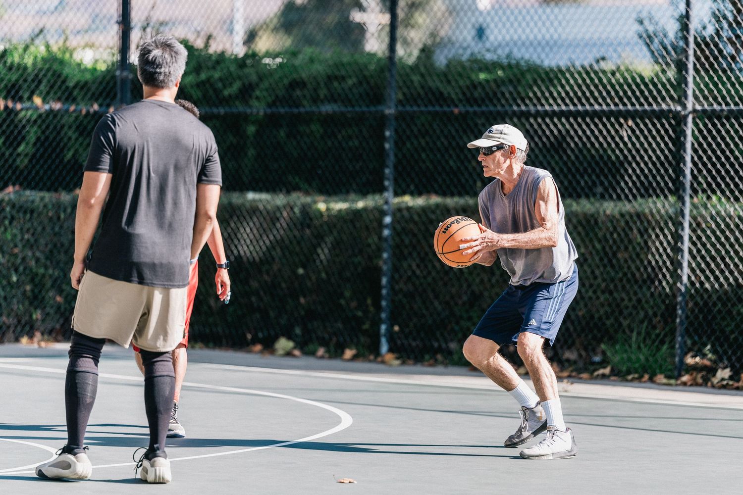 Two players engaged in a one-on-one basketball game on an outdoor court with mountains in the background.