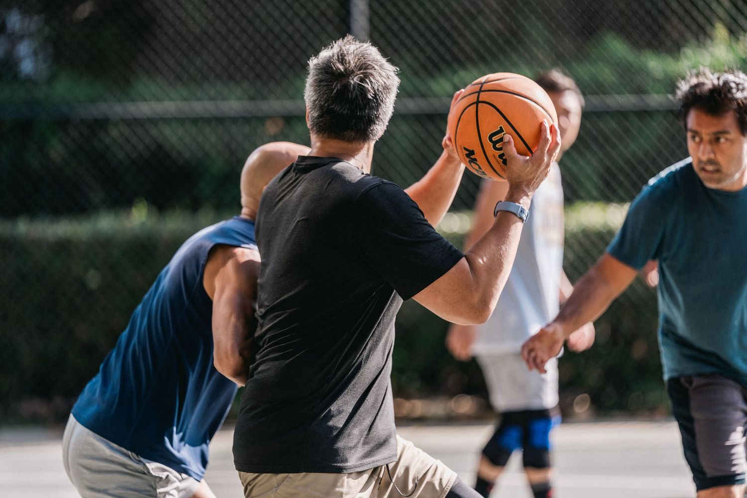 Players dribble and defend during an intense outdoor basketball game on a sunny day.