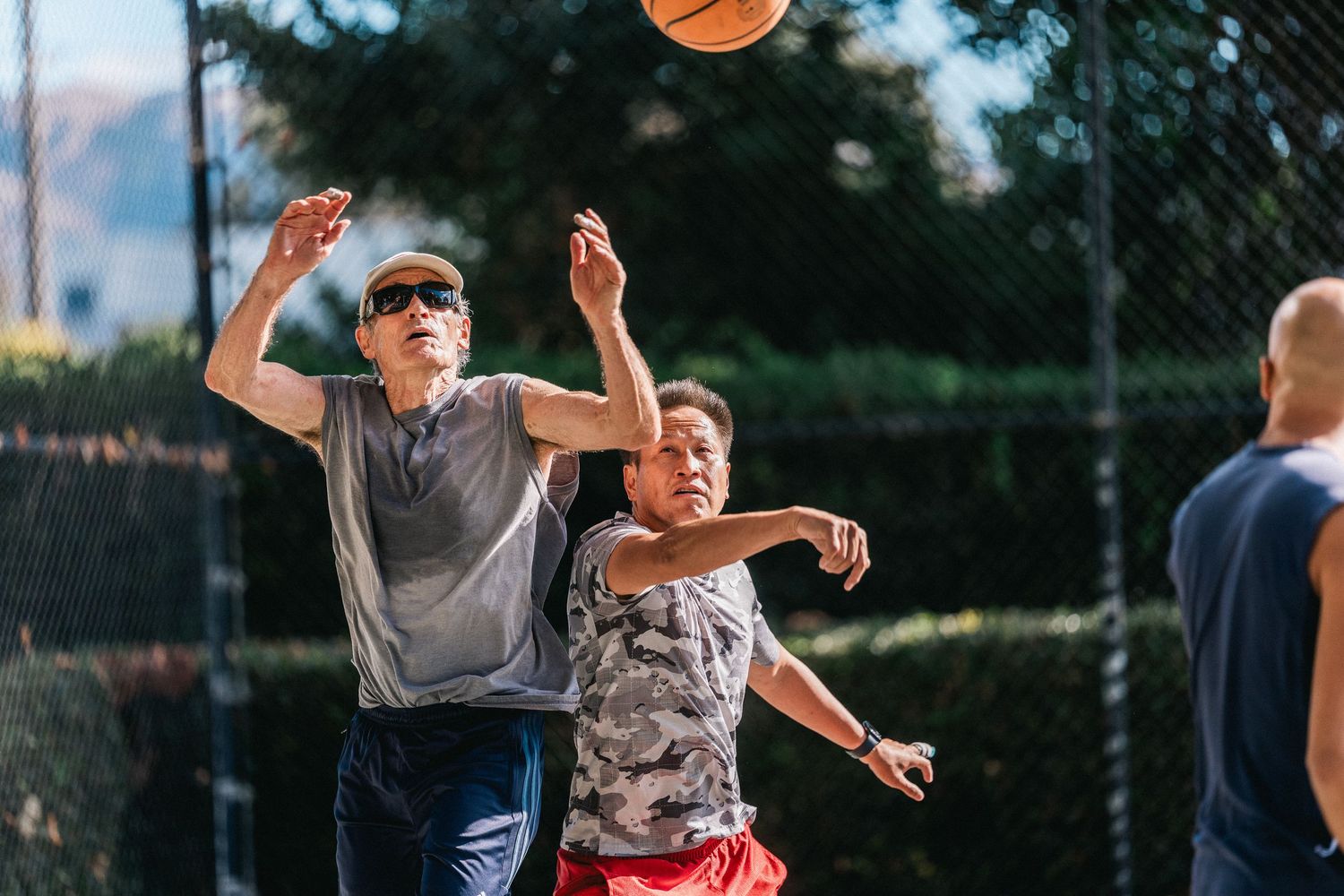 Players jumping to catch a basketball during a casual outdoor game on a sunny day.