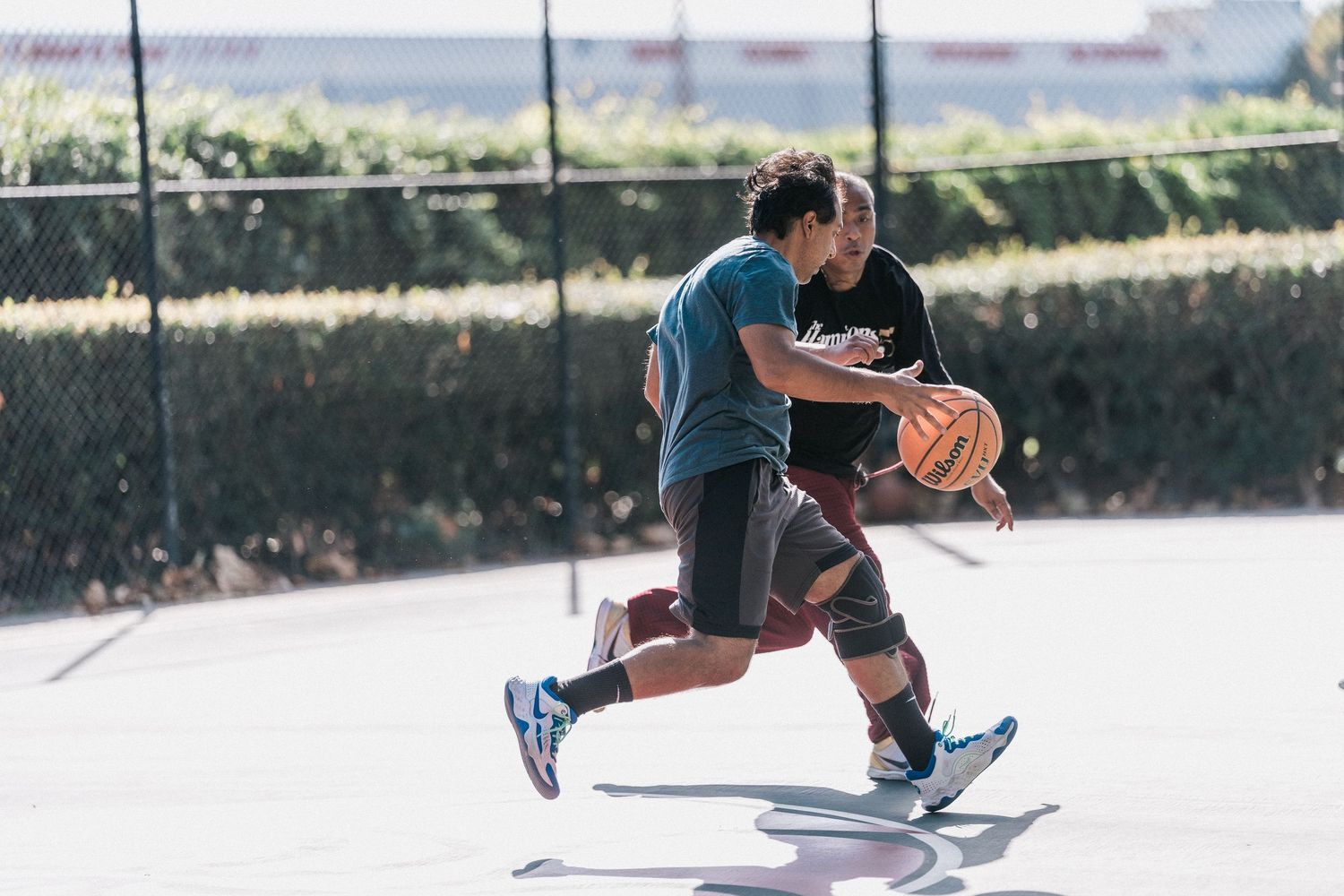 Basketball players jump and compete for the ball during an intense outdoor game on a sunny court.