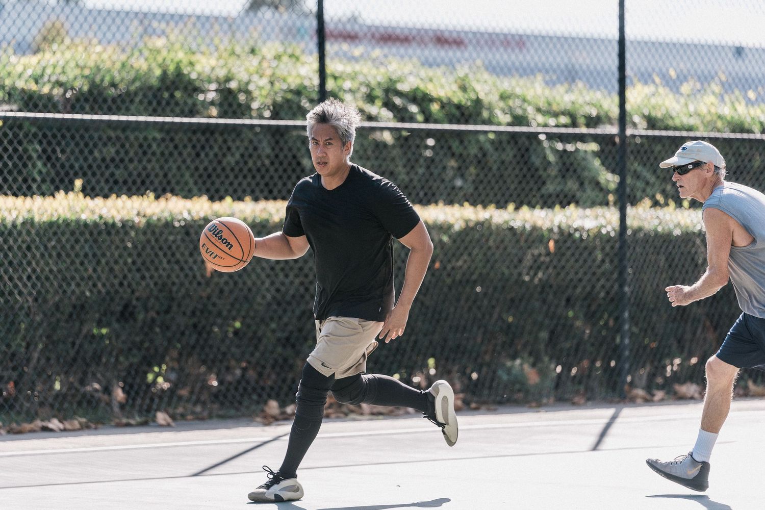 Players engaged in an intense basketball game on an outdoor court with chain link fencing.