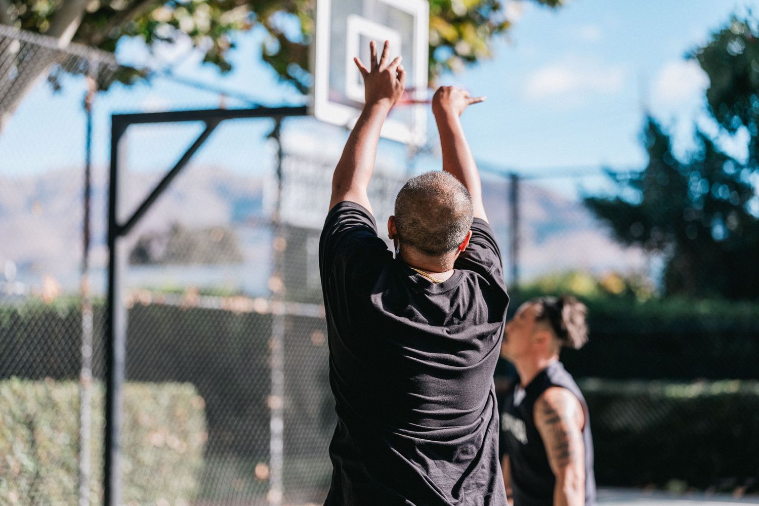 Basketball players in action on a sunny court with mountains visible in the background.