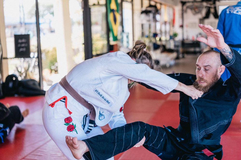Athletes practicing Brazilian Jiu-Jitsu techniques on red mats during a training session.