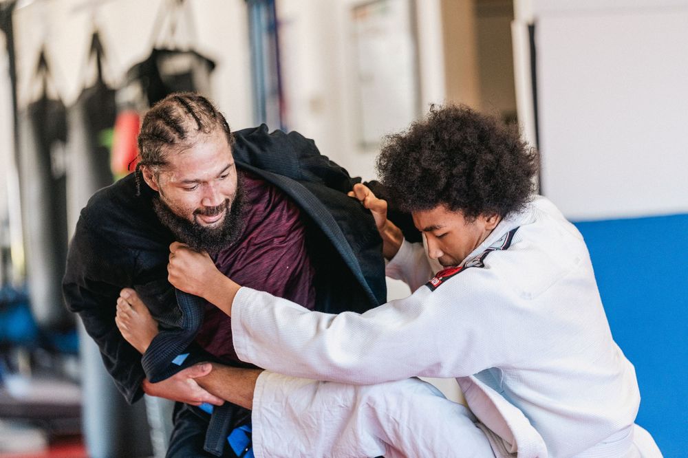 Two martial arts practitioners in white gis practice grappling techniques during jiu-jitsu training.