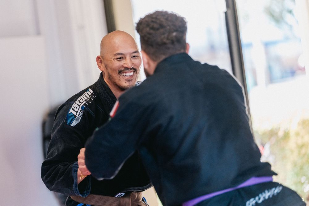 Two people in black gis practicing Brazilian Jiu-Jitsu techniques during a training session.