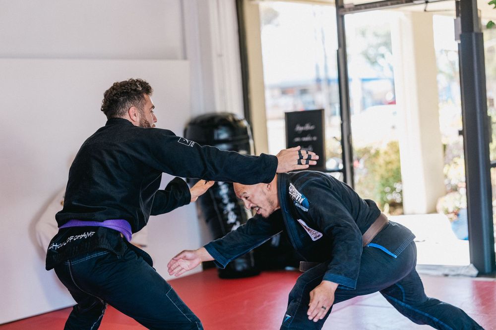 Students practicing martial arts techniques in a training sequence on red mats in a dojo.