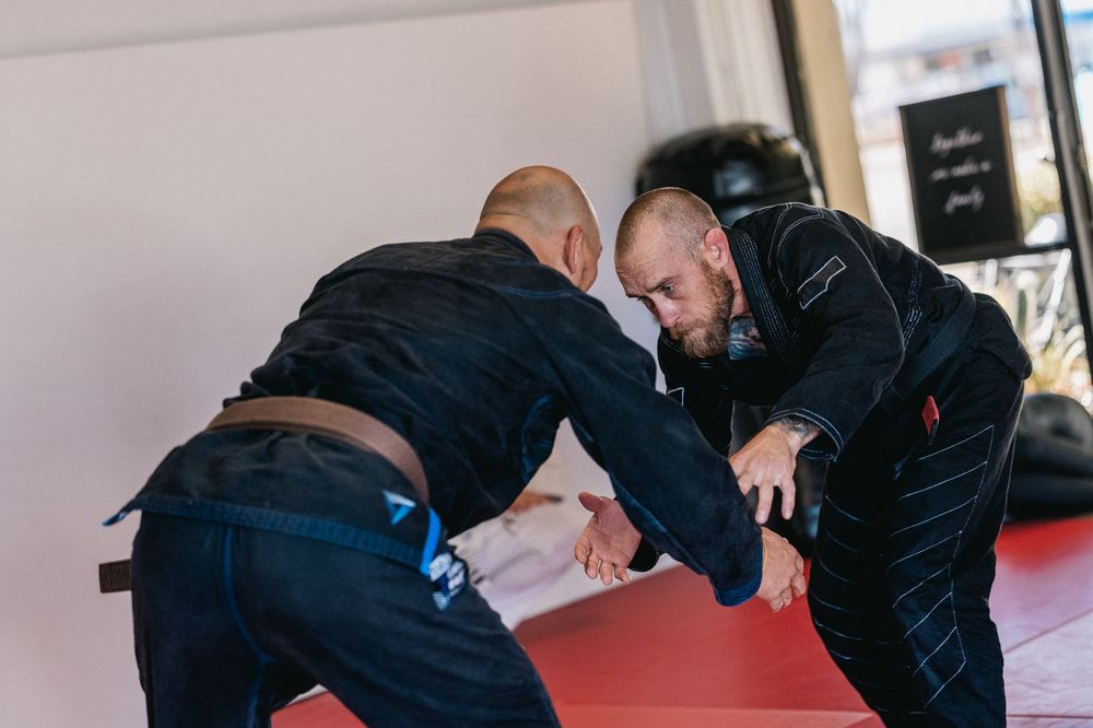 A series of martial arts students practicing grappling techniques on red mats during a training session.