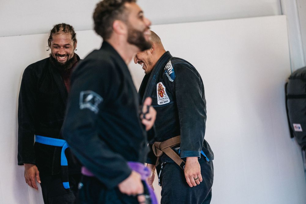 Two martial artists practicing grappling techniques on a mat while wearing black gis during training.