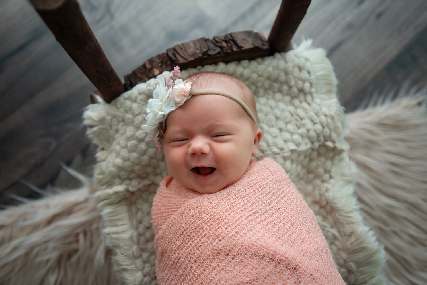 A sleeping newborn wrapped in a soft pink swaddle blanket lies on a white textured blanket.