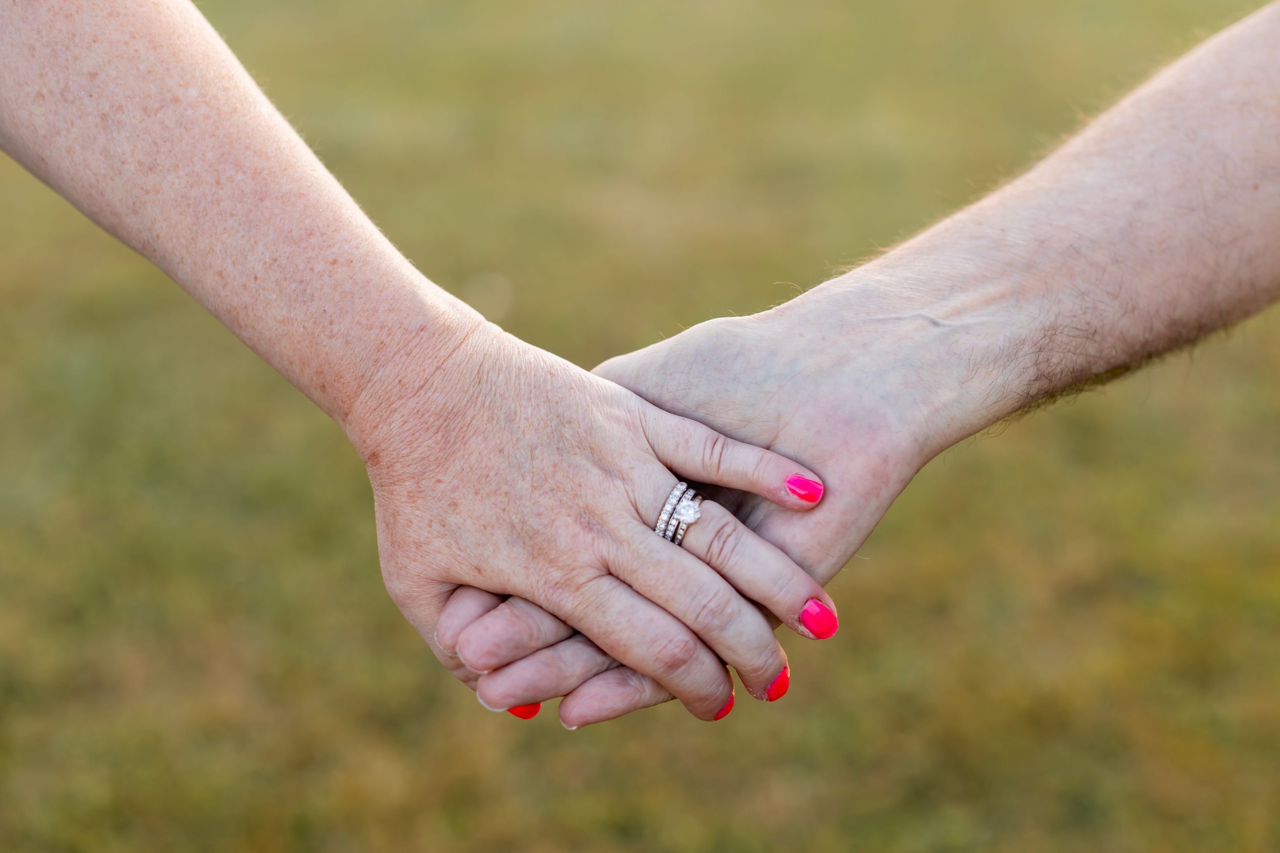 Close-up view of two hands reaching out to hold each other against a soft blurred outdoor background. NJ extended family photographer