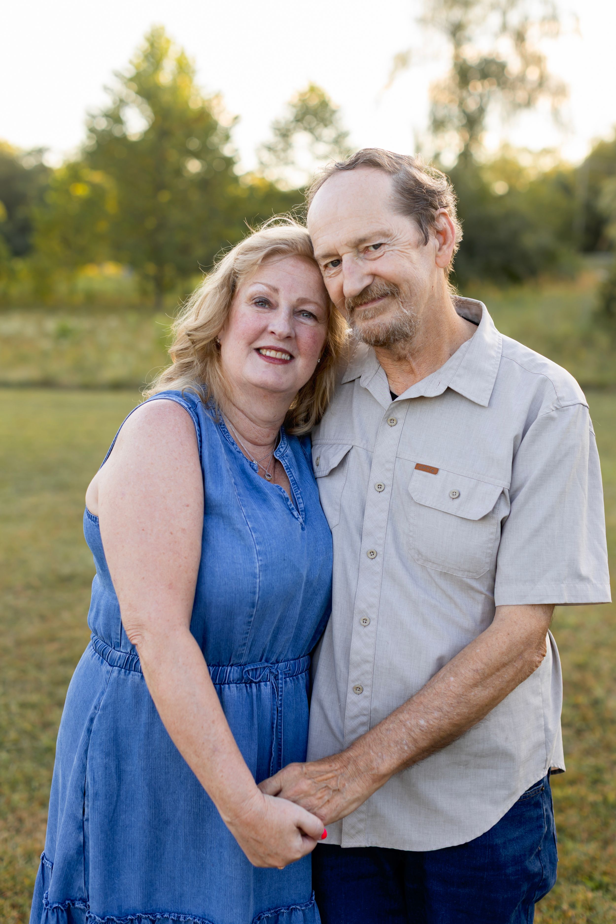 Couple embracing outdoors in casual attire against a sunlit natural background. NJ extended family photographer