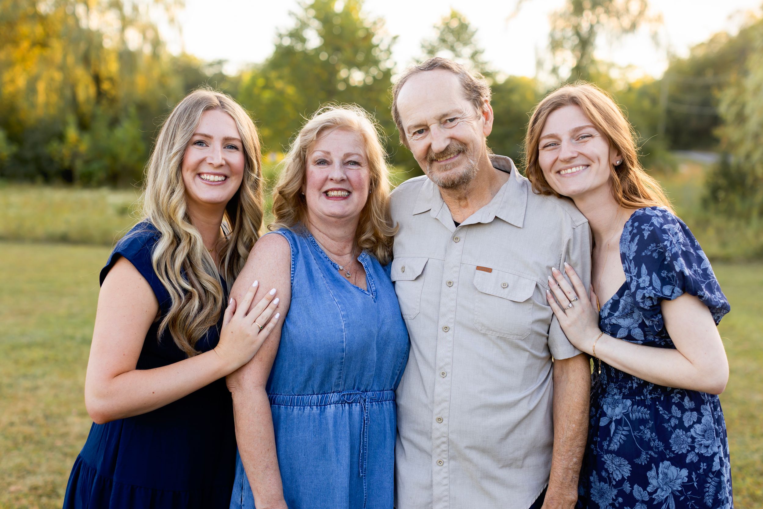 A group in coordinating blue outfits poses together on a grassy field during golden hour. NJ extended family photographer