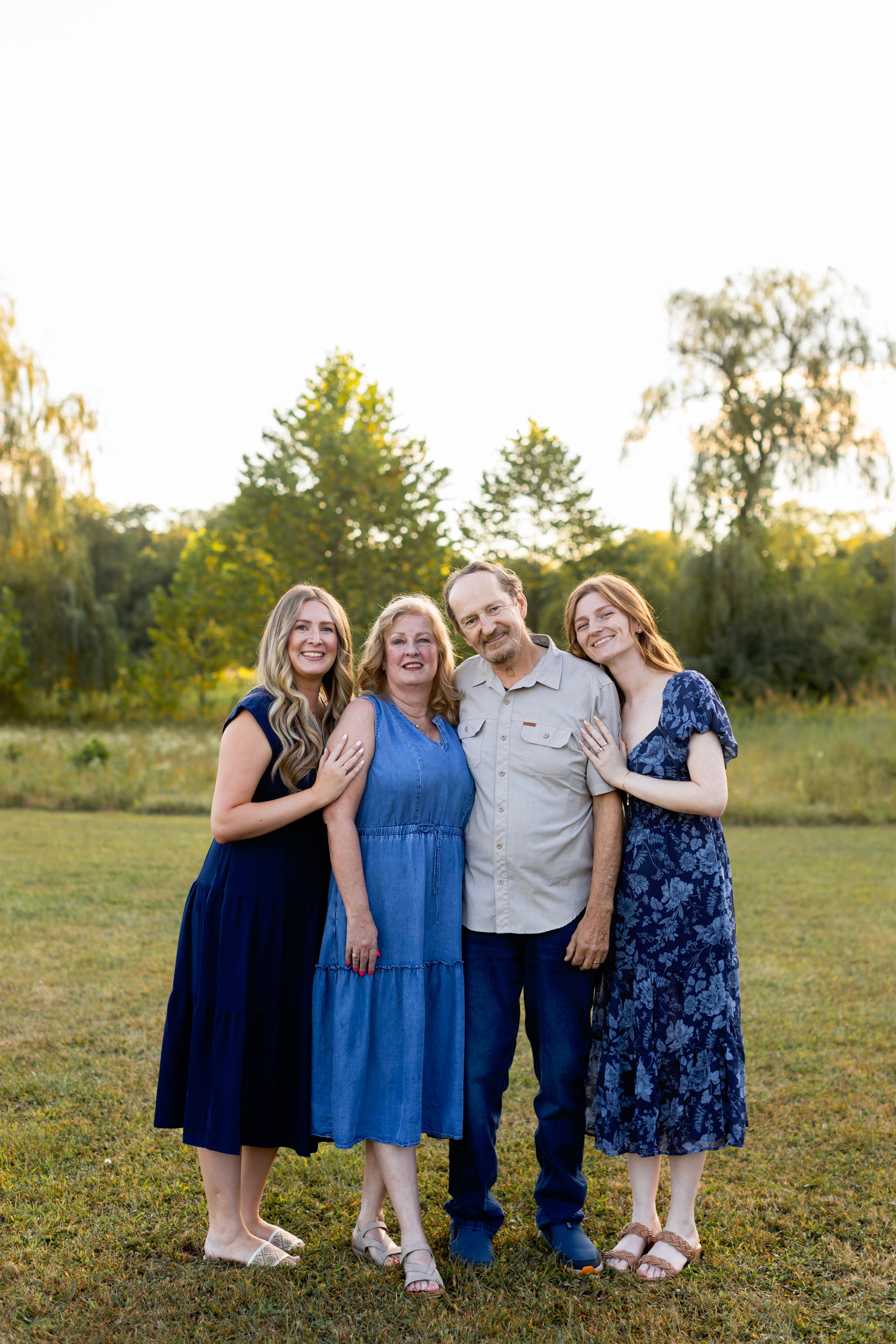Family members in navy and blue dresses stand together on grass during sunset. NJ extended family photographer