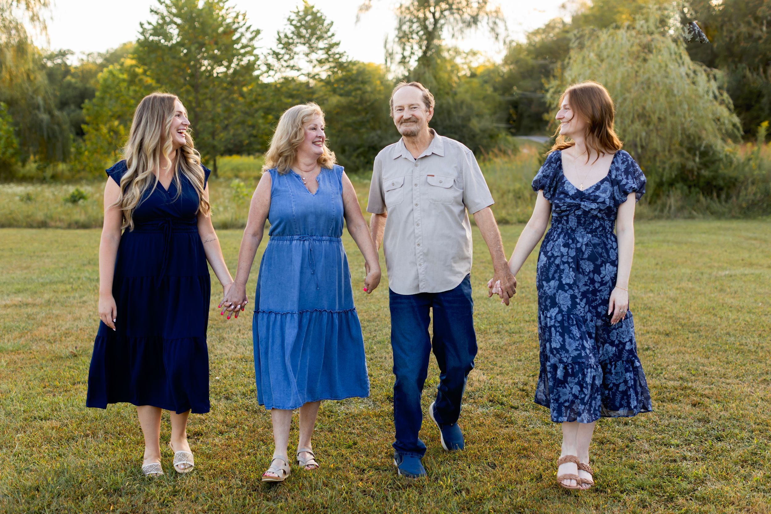 A group walks together through a grassy field at sunset wearing coordinating blue and navy outfits. NJ extended family photographer
