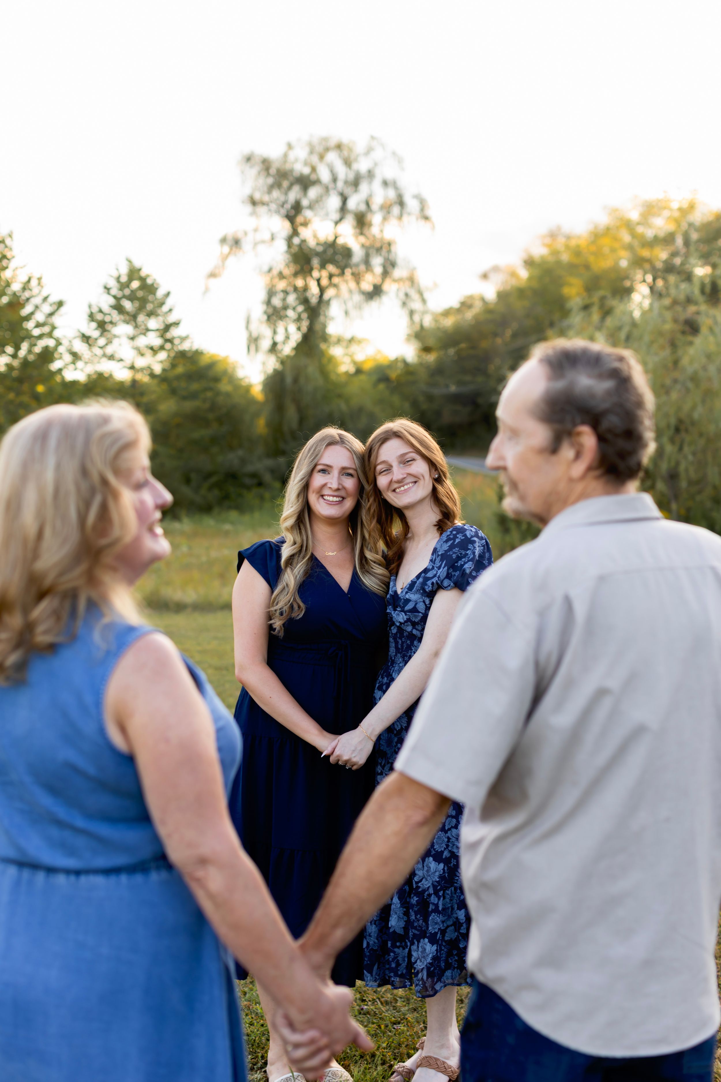 A joyful family wearing coordinated blue and neutral outfits laughs together during an outdoor photo session. NJ extended family photographe