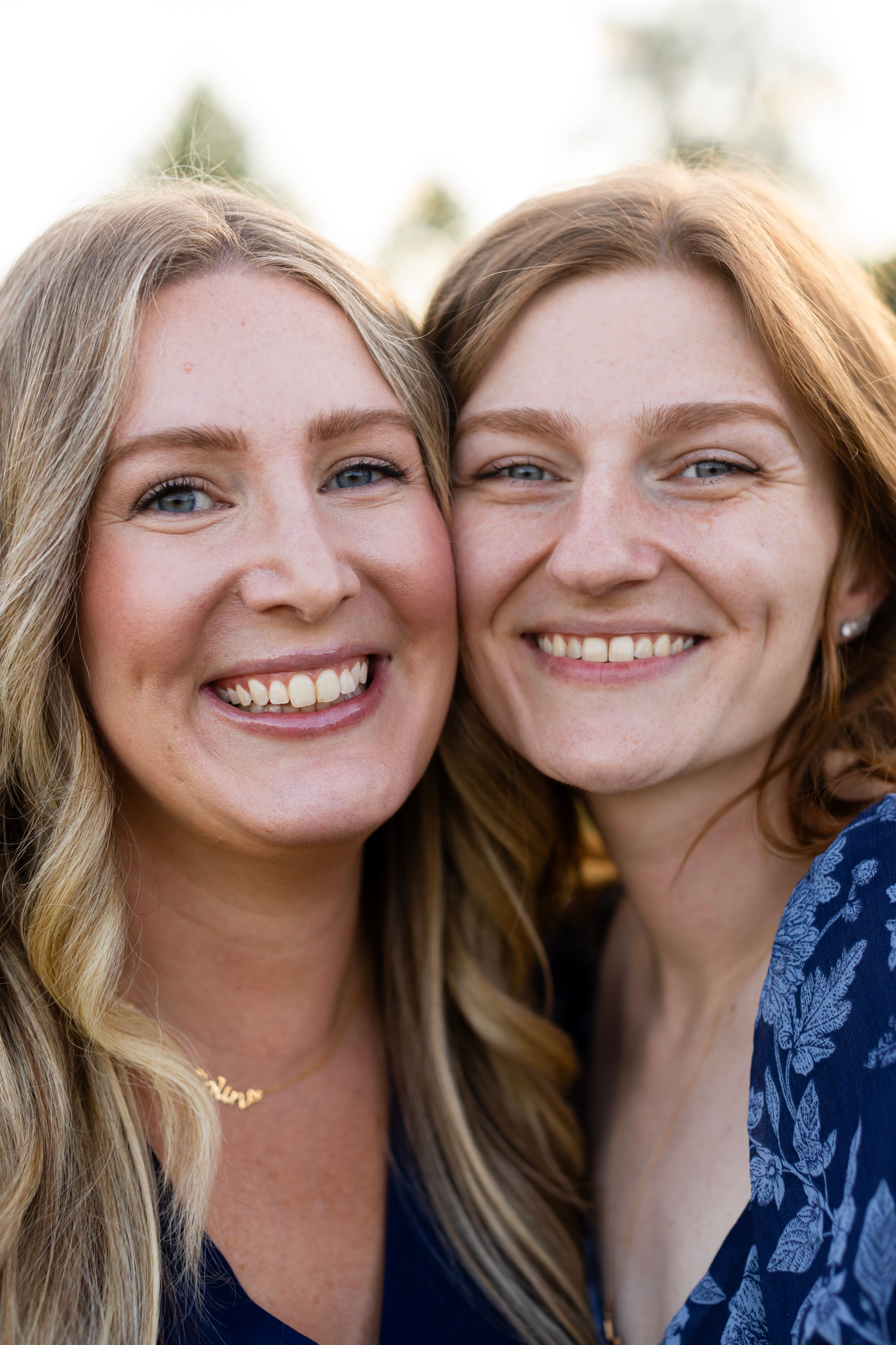 Two women with blonde hair share a close moment while smiling at the camera outdoors. Sussex County NJ Photographer