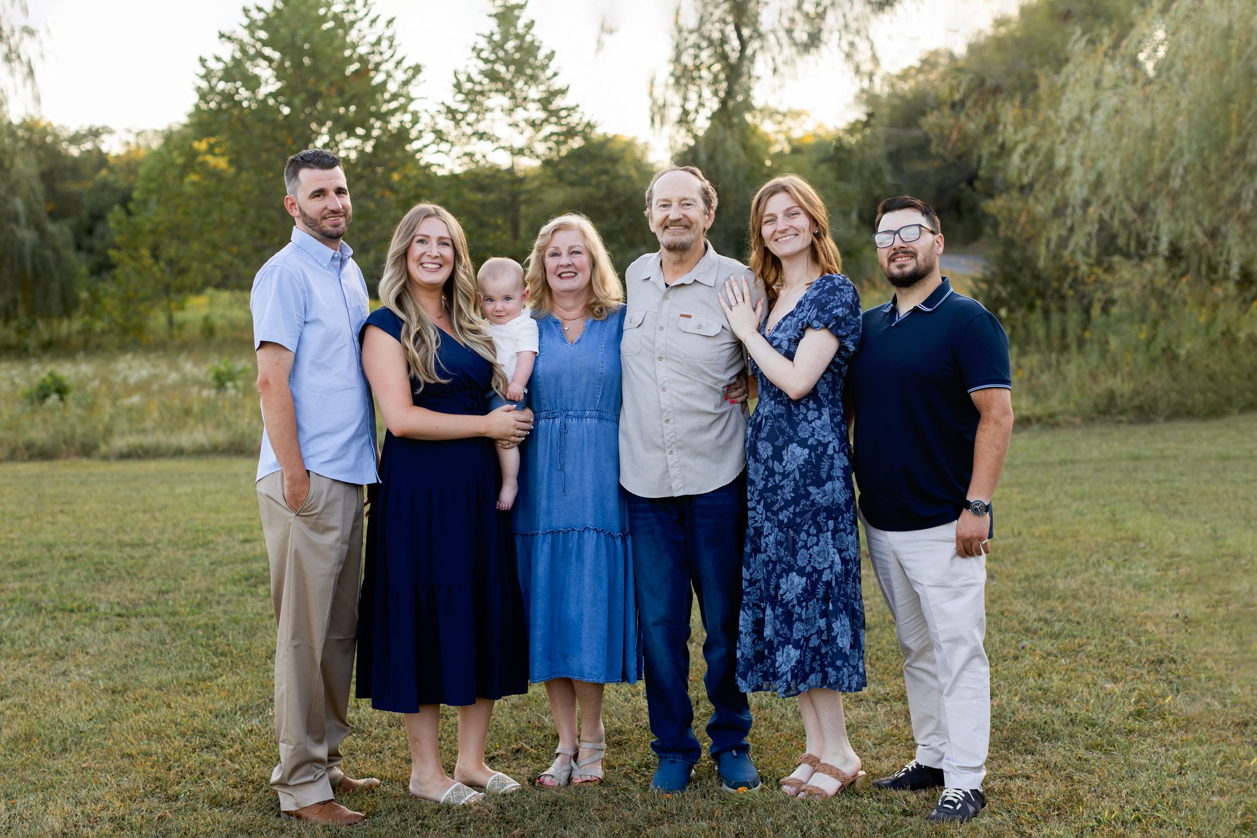 Extended family wearing blue and white outfits poses together outdoors during golden hour photography session. Sussex County NJ Photographer
