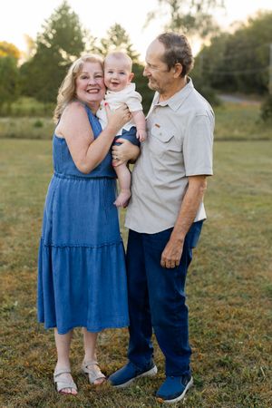 Three people pose together on grass during a golden hour photoshoot wearing blue and neutral tones.
