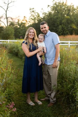 A family in coordinated navy and light blue outfits poses together in a sunlit meadow during golden hour.