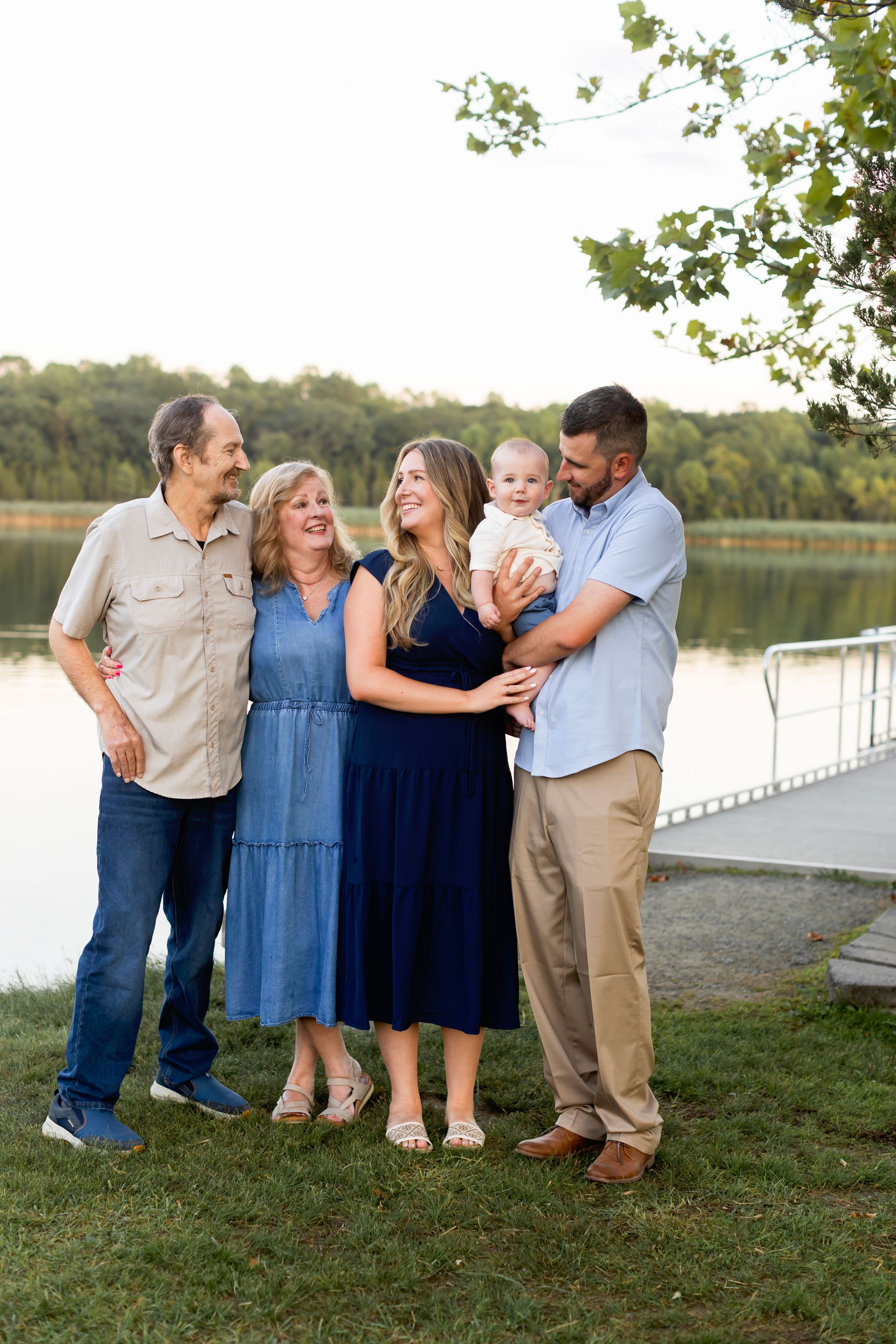 Family group poses along a lakeside path while sharing embraces and smiles at sunset.