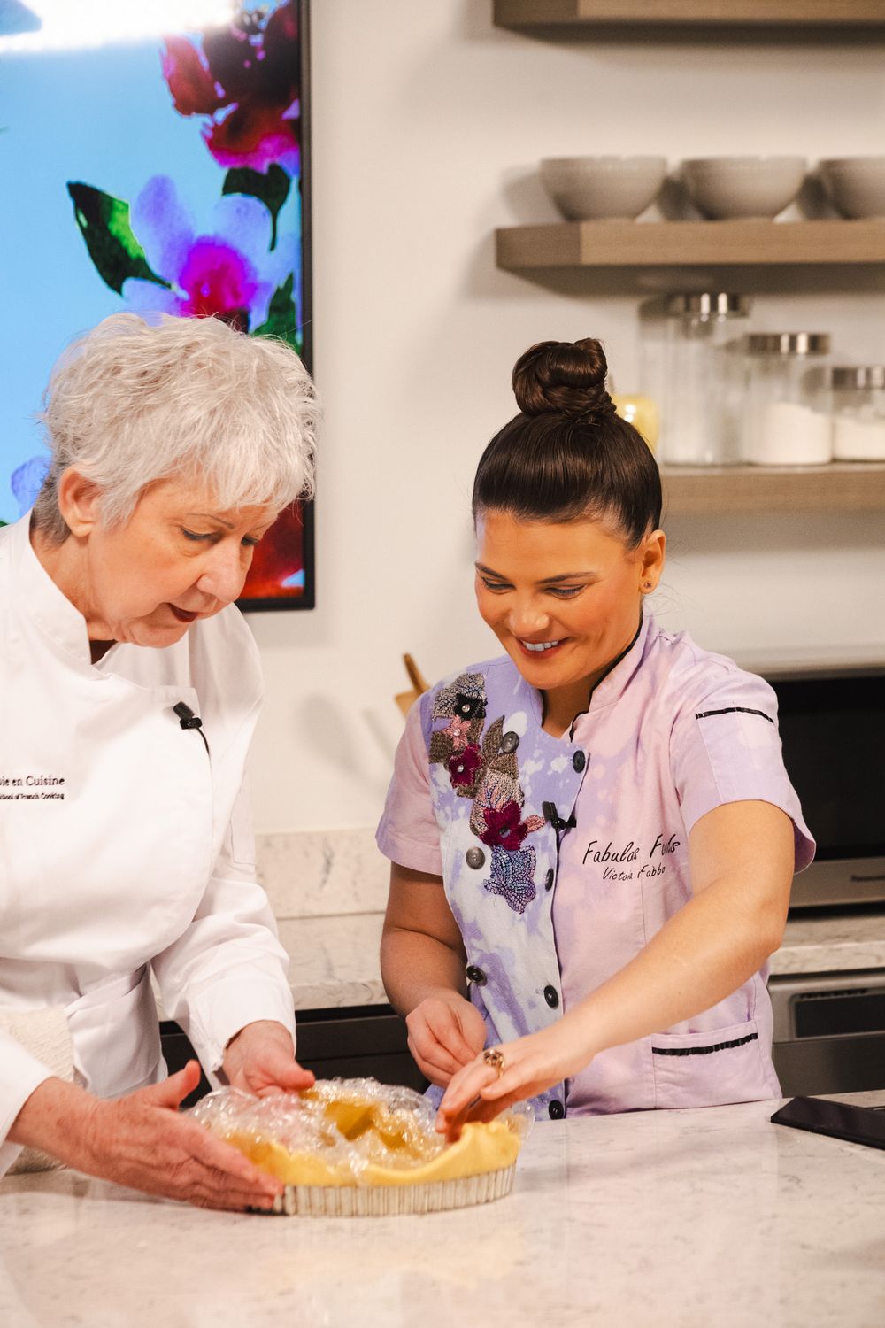 Two chefs in white uniforms work together to decorate a pie with whipped cream in a bright kitchen setting.