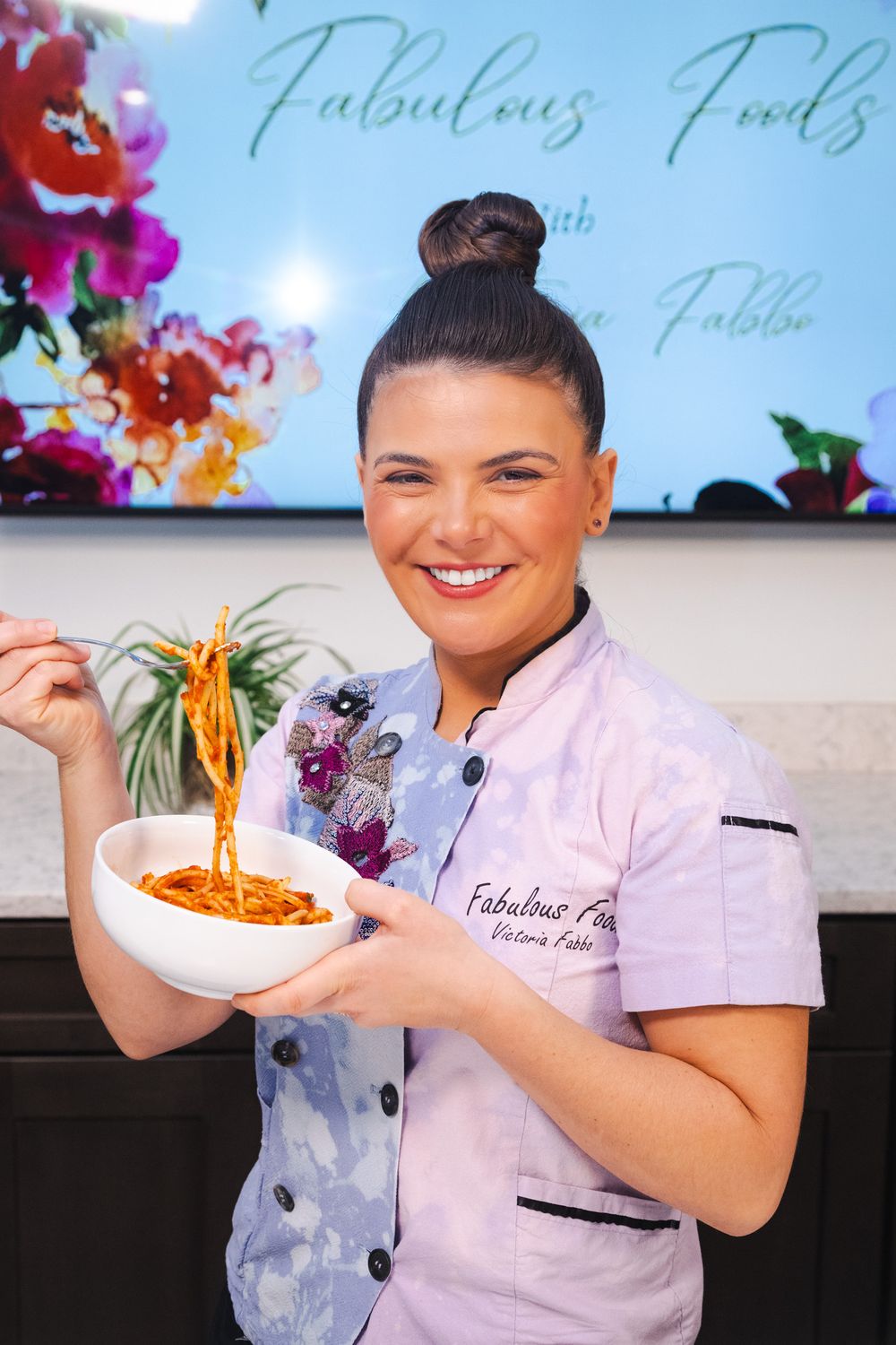 Chef in white uniform demonstrates noodle pulling technique with colorful background display.