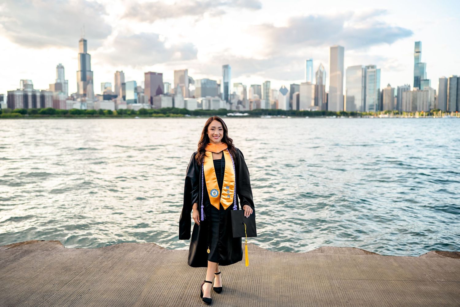 A person in a black leather jacket and yellow scarf poses along Lake Michigan with Chicago's skyline in the background.