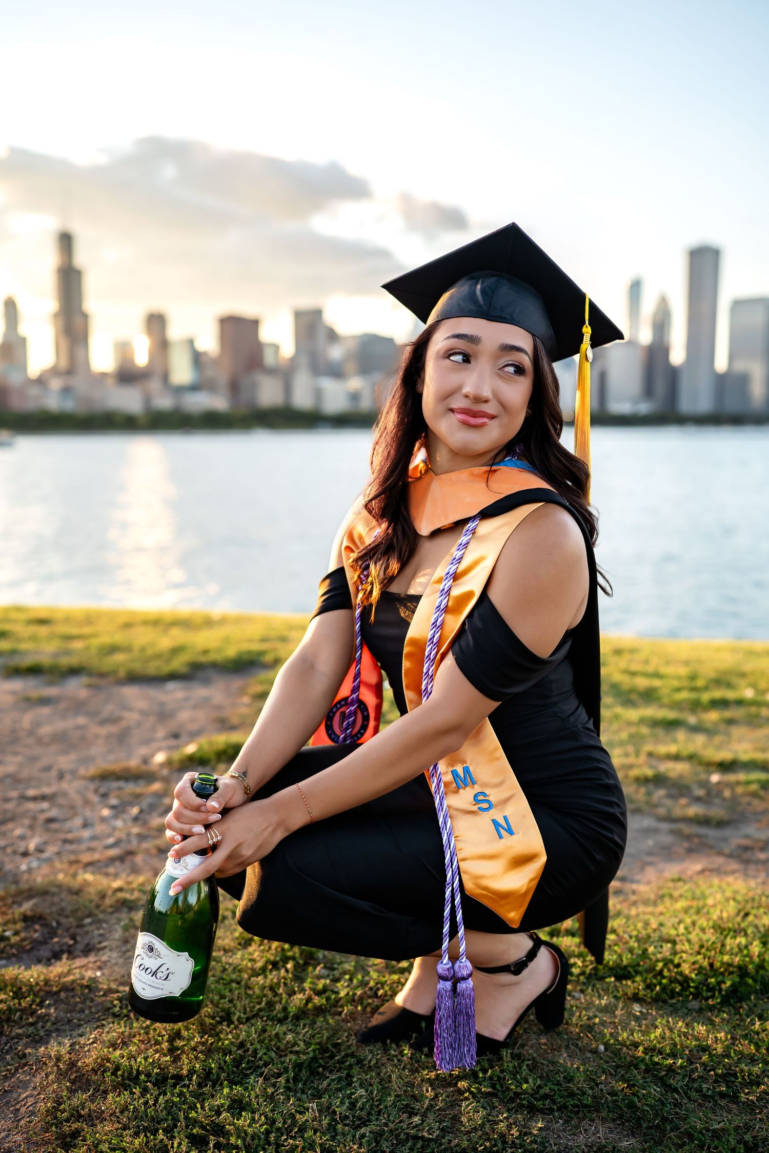 A graduate in cap and gown poses by the Miami skyline at sunset for a series of graduation photos on the waterfront.