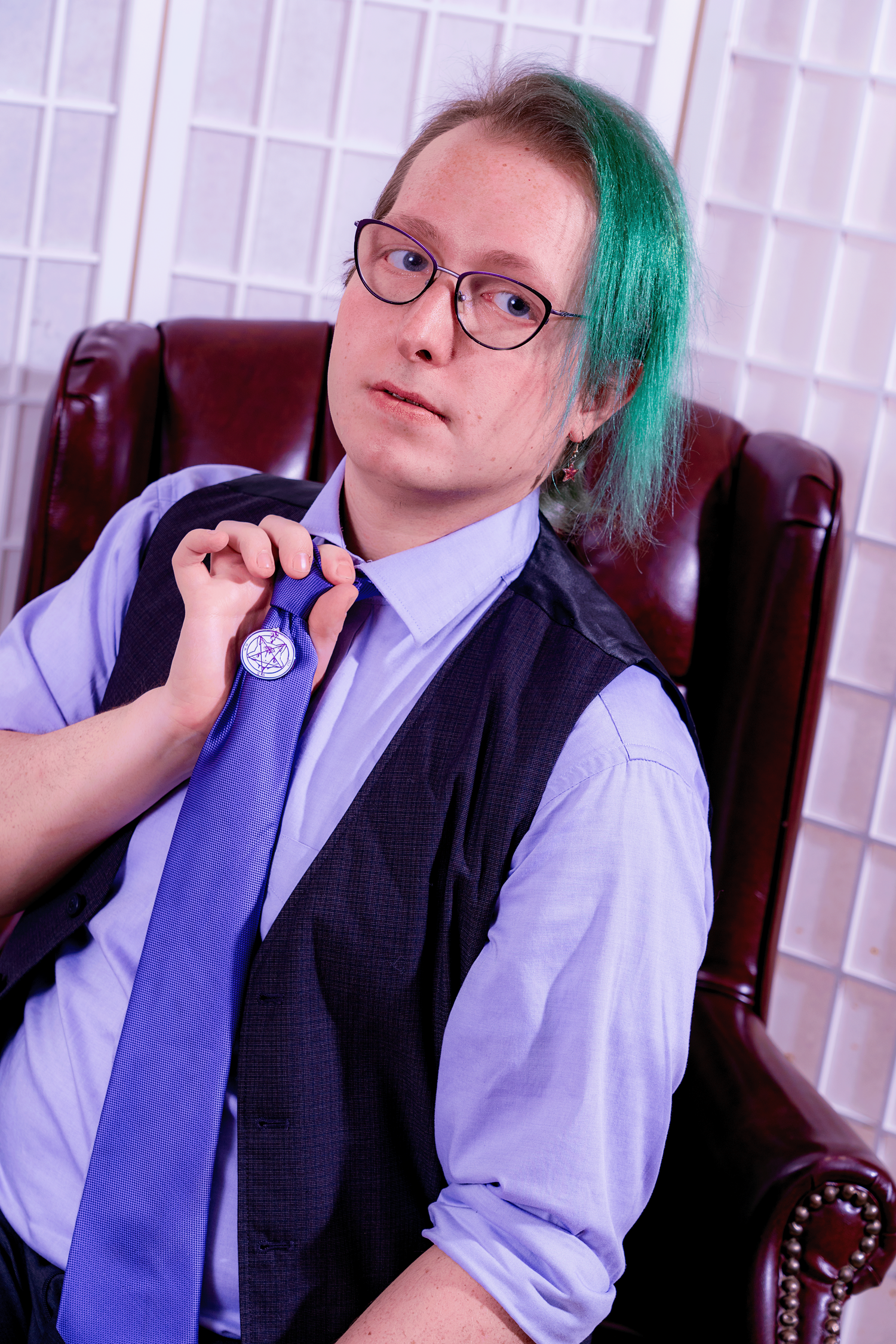 Rorianna Seht, owner of the Seht Up in a purple shirt and tie as she poses in a regal red chair