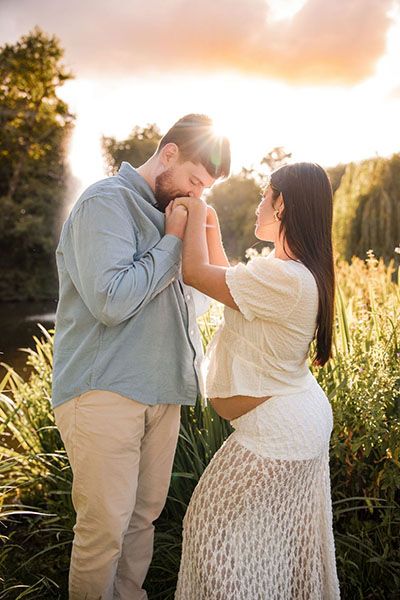 Romantic pregnant couple shares tender moment in golden sunlit field with tall grass during sunset photoshoot in Amsterdam.