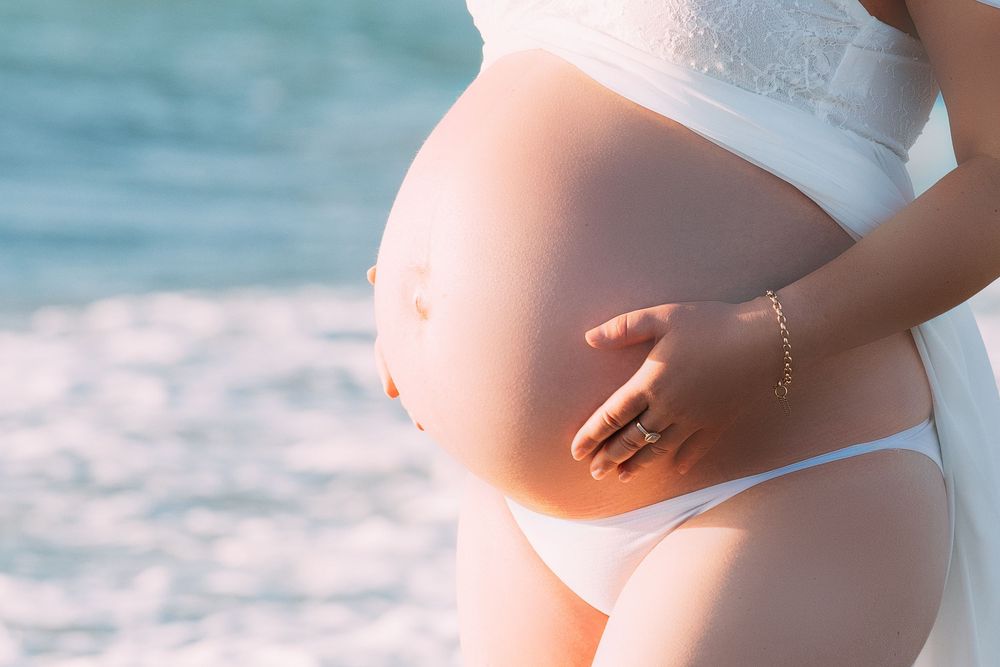 A series of maternity photos showing a pregnant belly in white clothing against a blue ocean background.