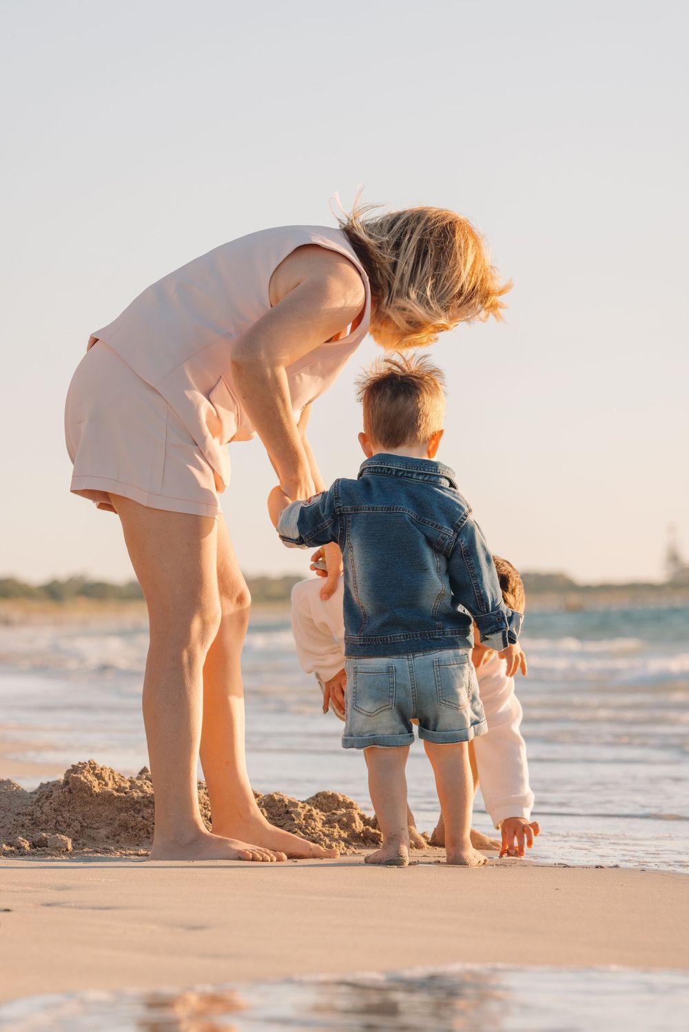 Parent and child explore seashells together on a sandy beach at sunset.