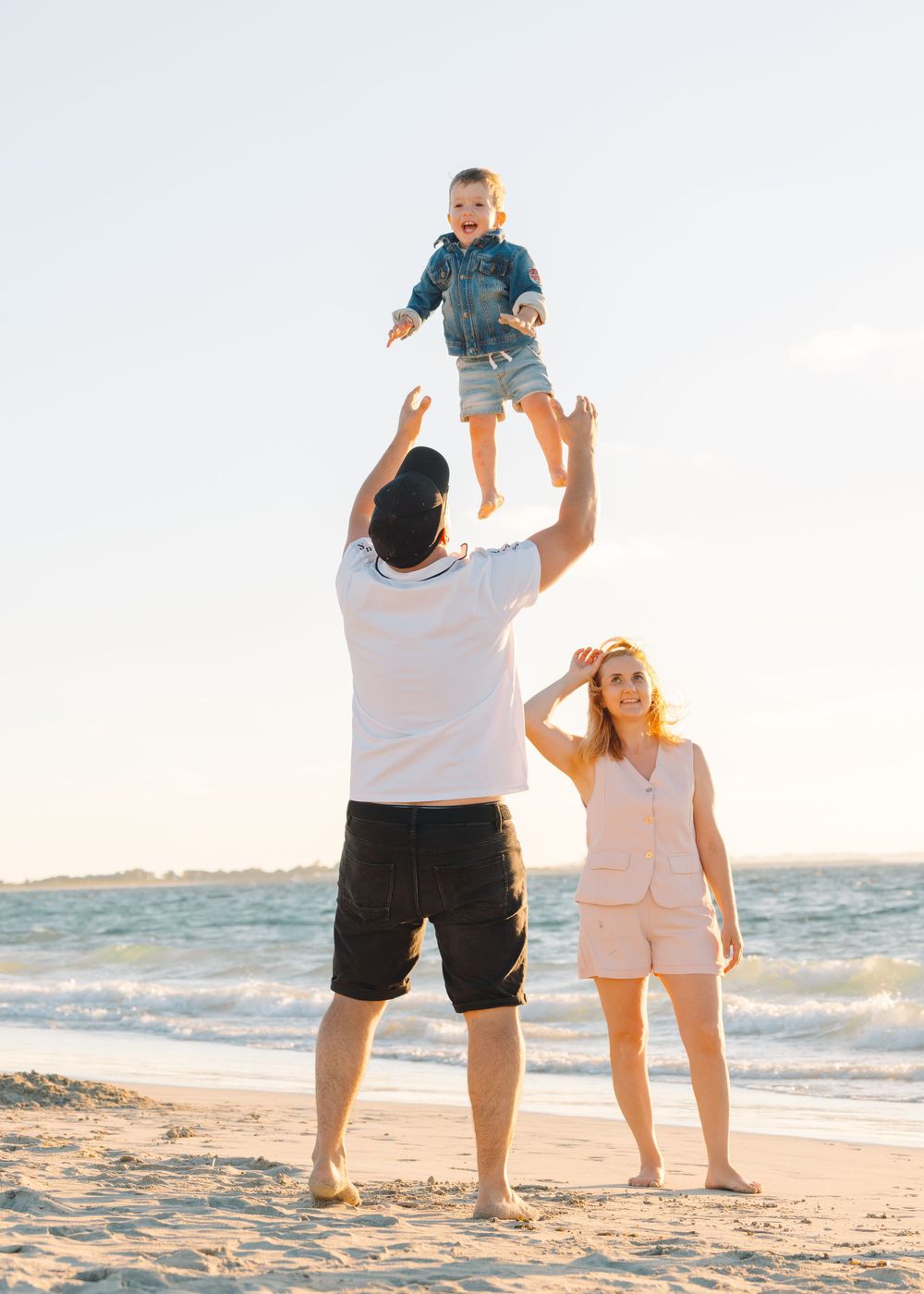Family enjoying a playful moment together on a sunny beach with waves in the background.